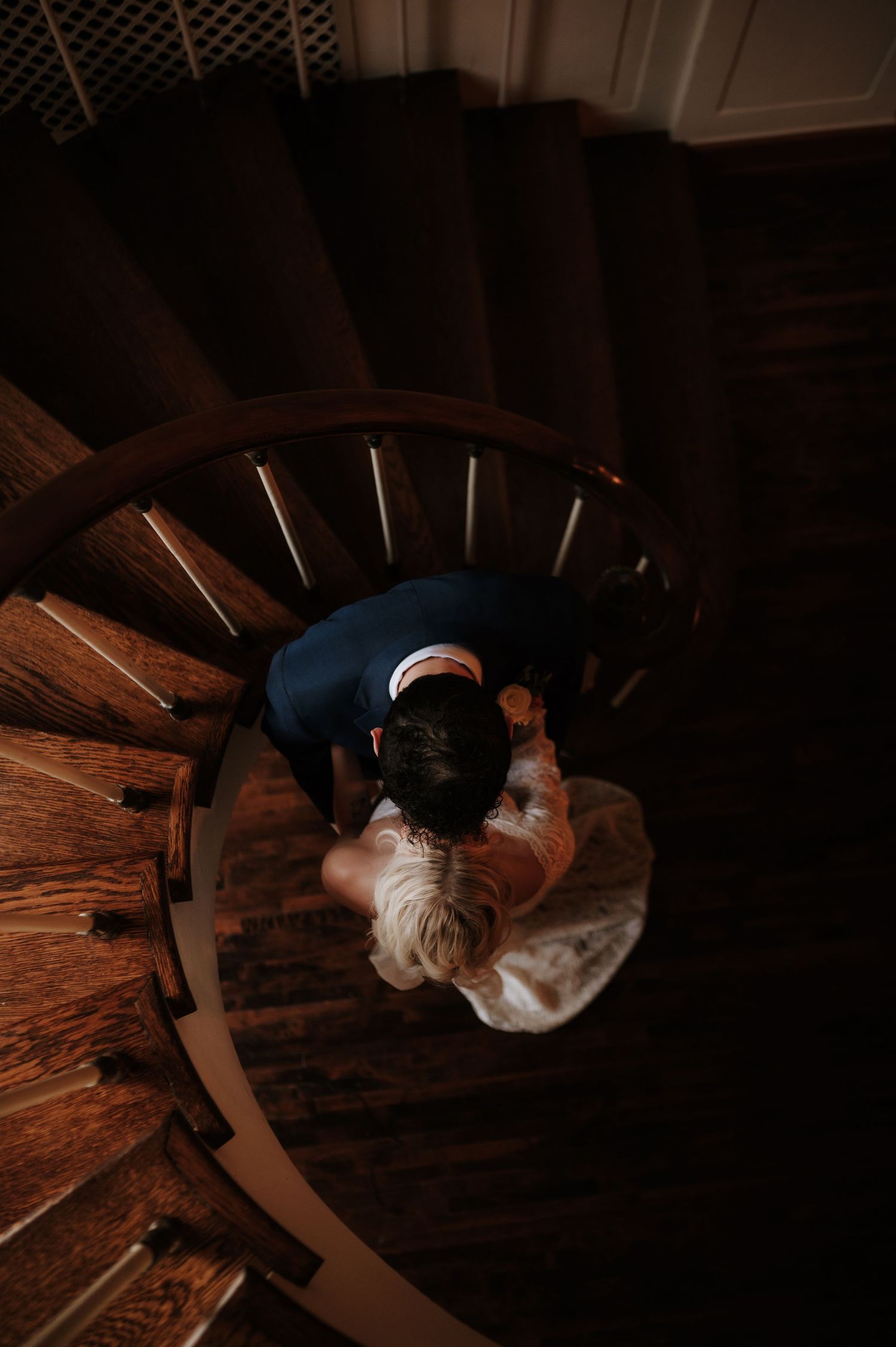 Artistic overhead spiral staircase shot in moody lighting at wedding venue.