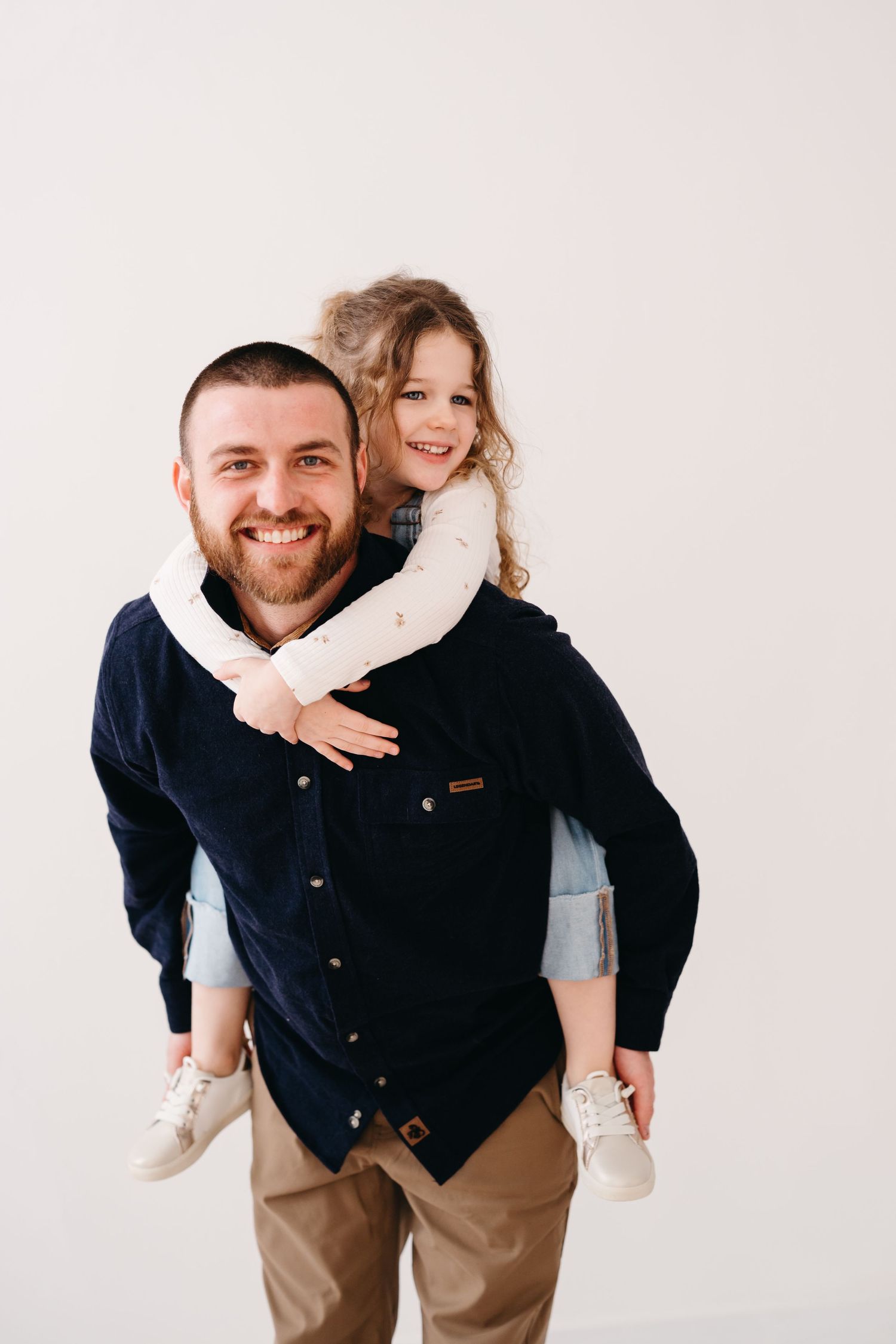 Parent giving piggyback ride to child in white sweater against light background.