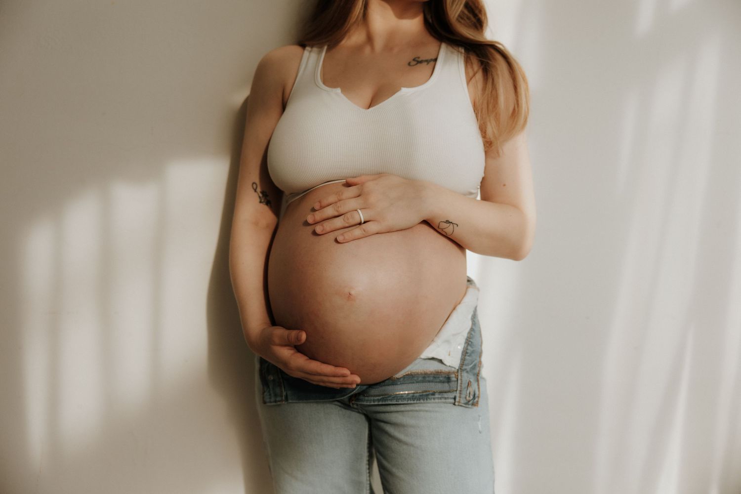 A series of maternity photos showing a pregnant belly in light jeans against a white backdrop.
