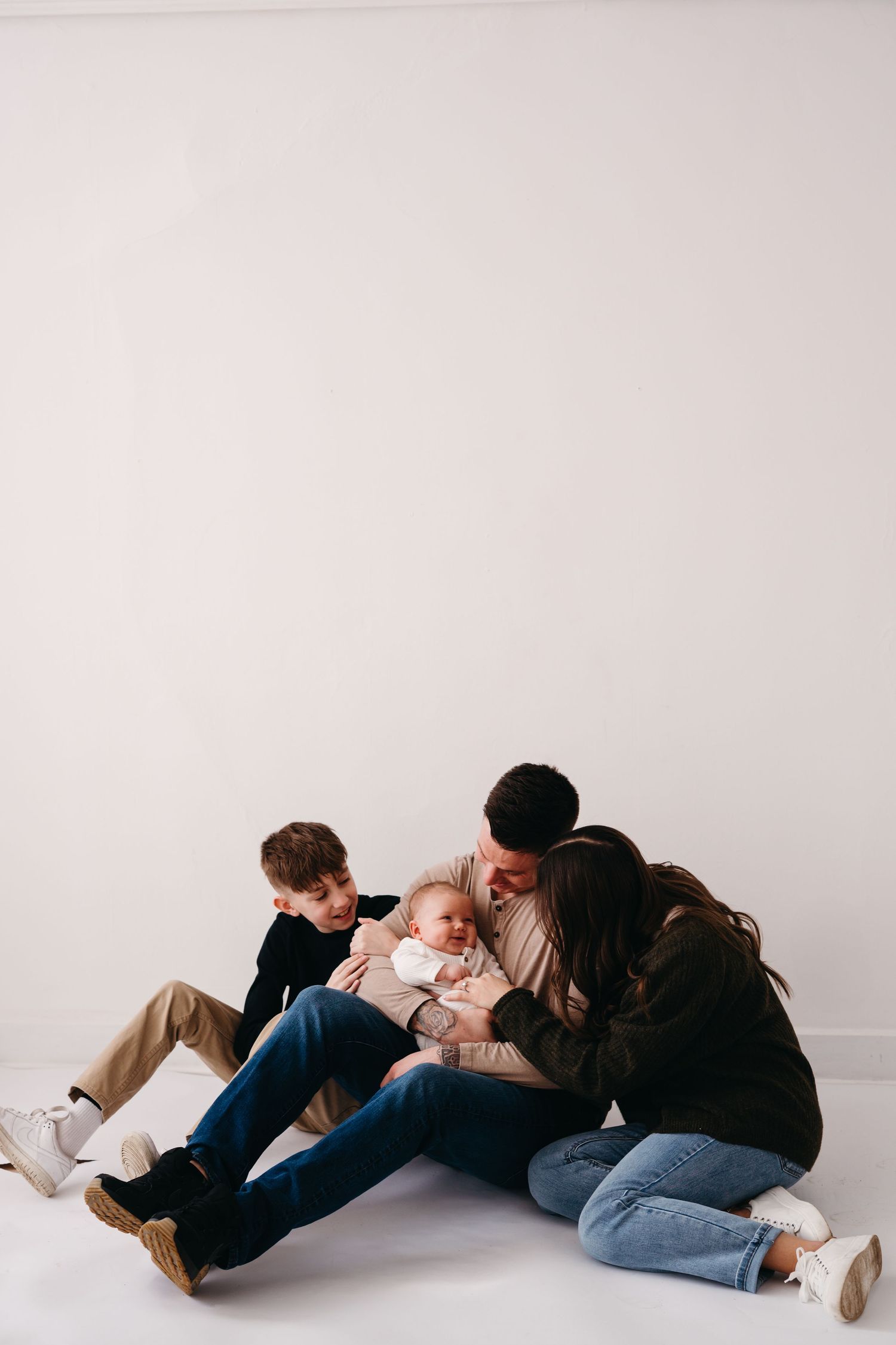A family sits together on the floor in an intimate moment against a white background.
