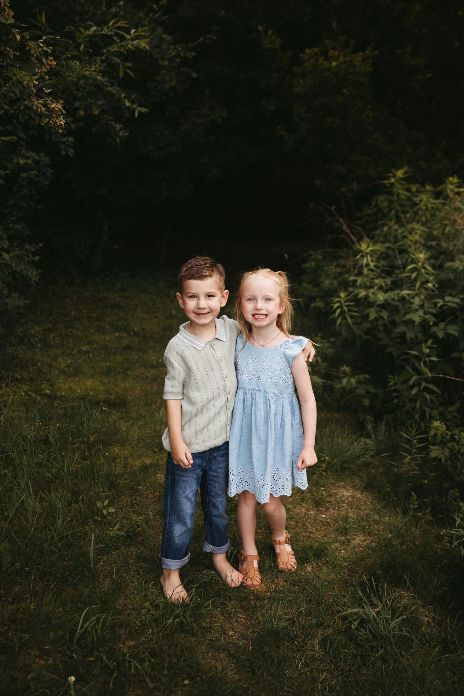 Two young children sitting side by side on grass wearing casual summer outfits.