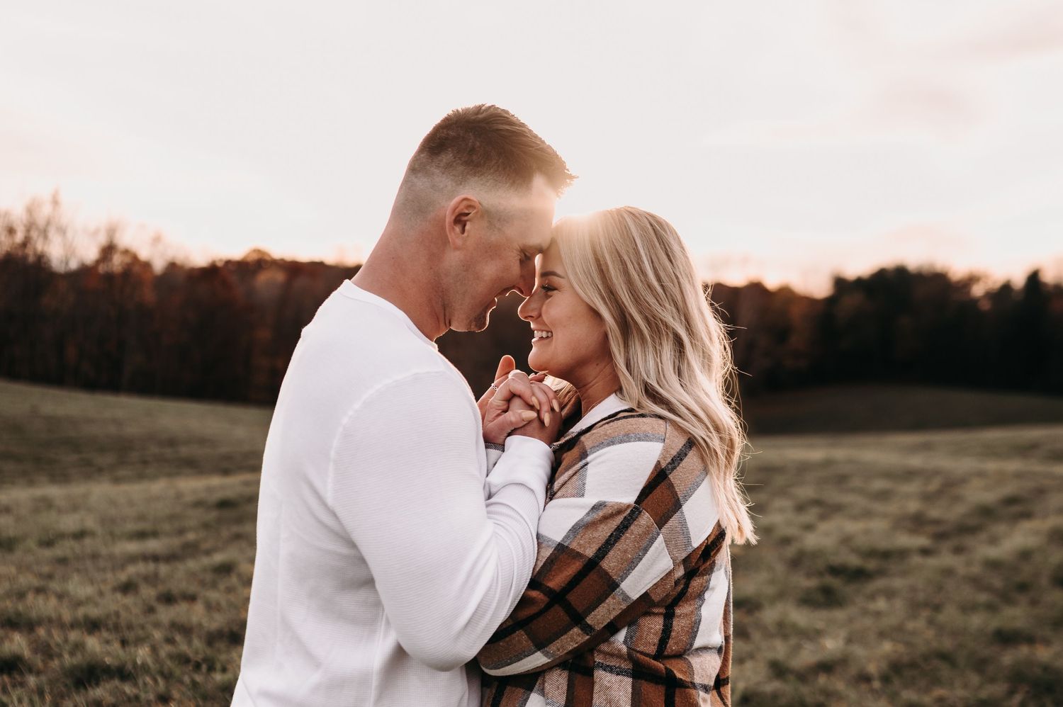 Tender moment between couple in rustic field during sunset.