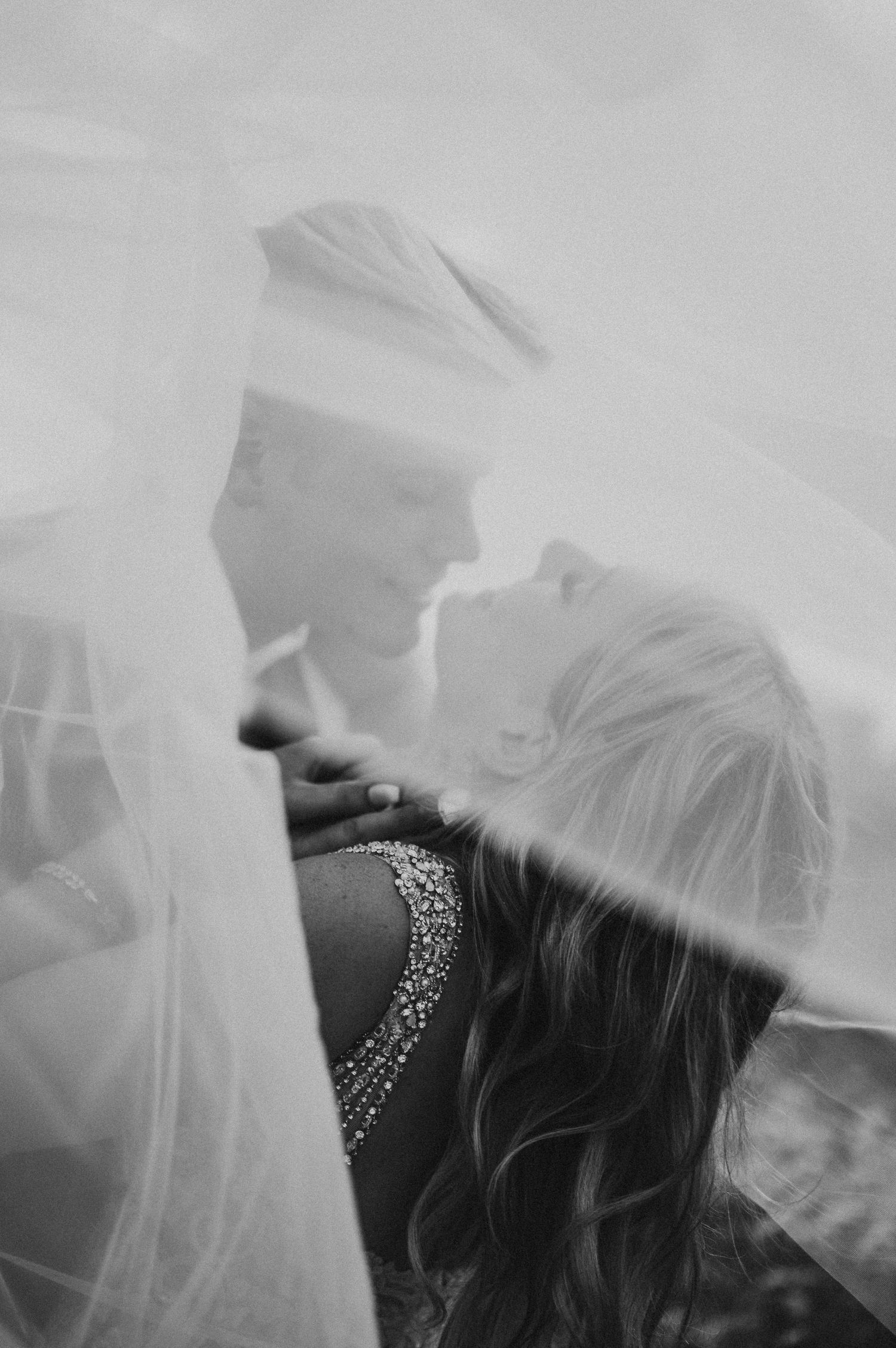 Ethereal black and white close-up portrait showing a delicate veil flowing in soft focus.