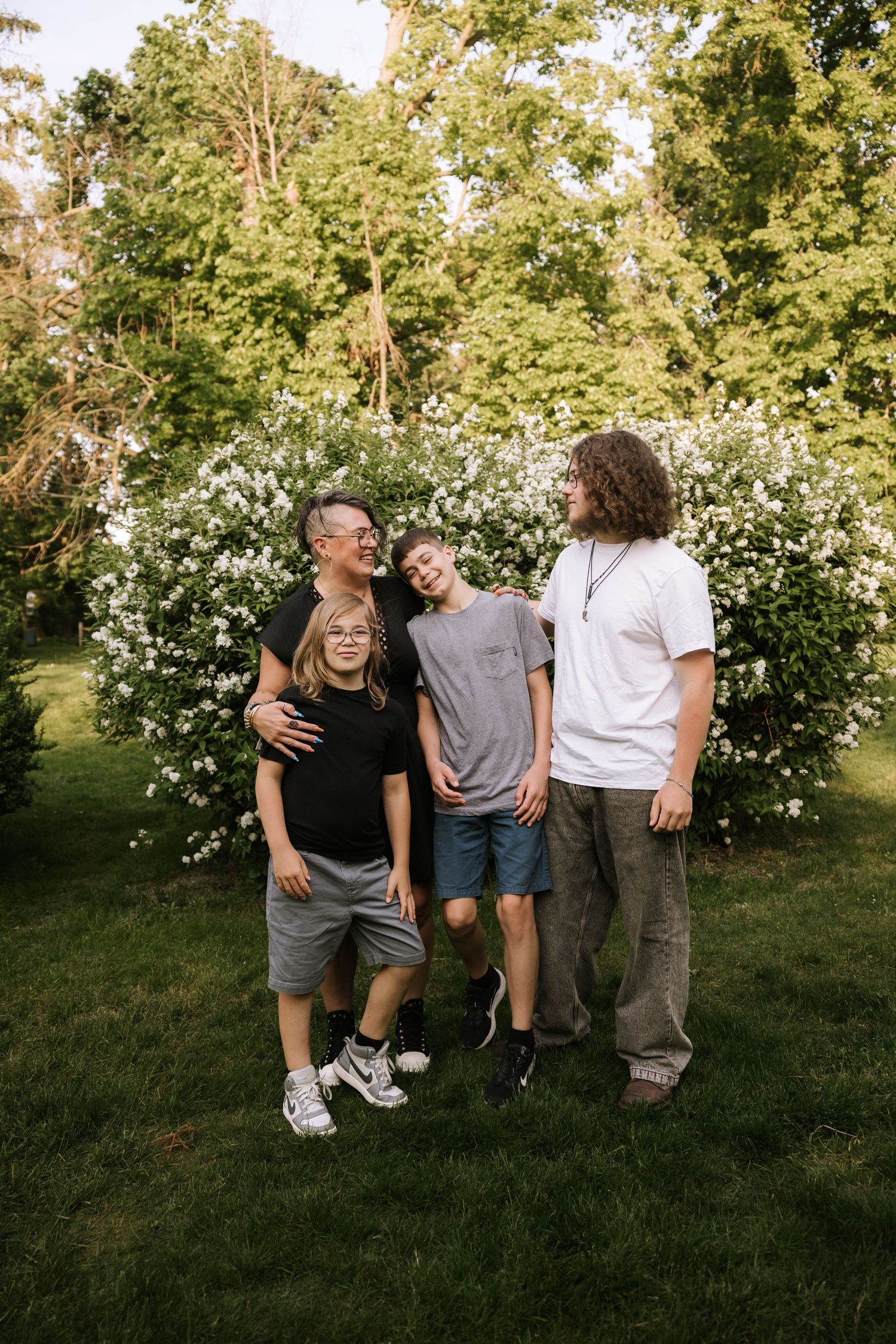 Family of four laughing together in front of white flowering bushes outdoors.