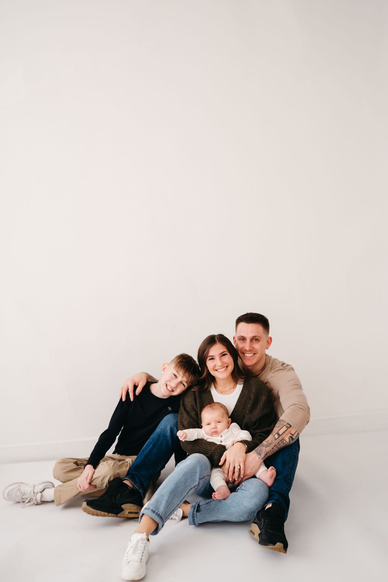 Modern family photo with everyone sitting close together against plain white wall.