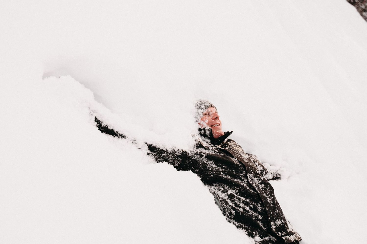 Person lying in snow with arms outstretched against white winter background.
