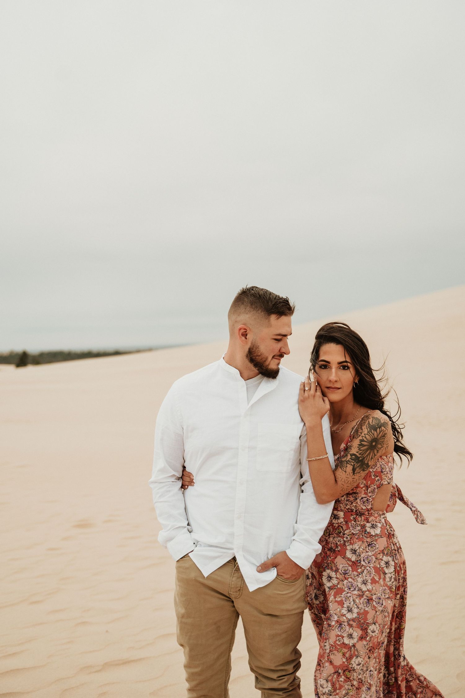 A couple in romantic desert photoshoot poses intimately against sandy dunes.