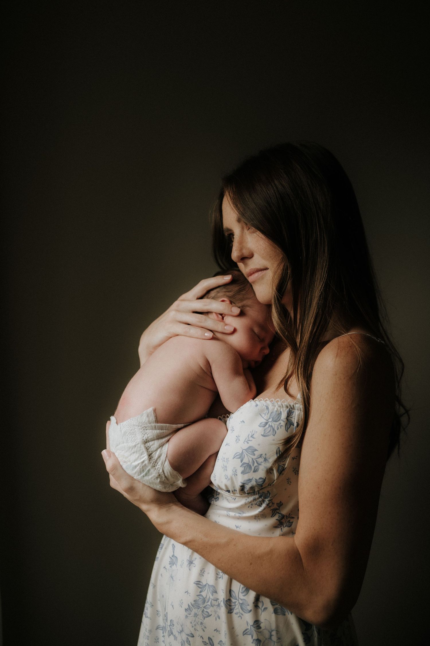 A tender moment captured in moody lighting with a mother cradling a newborn against her chest.