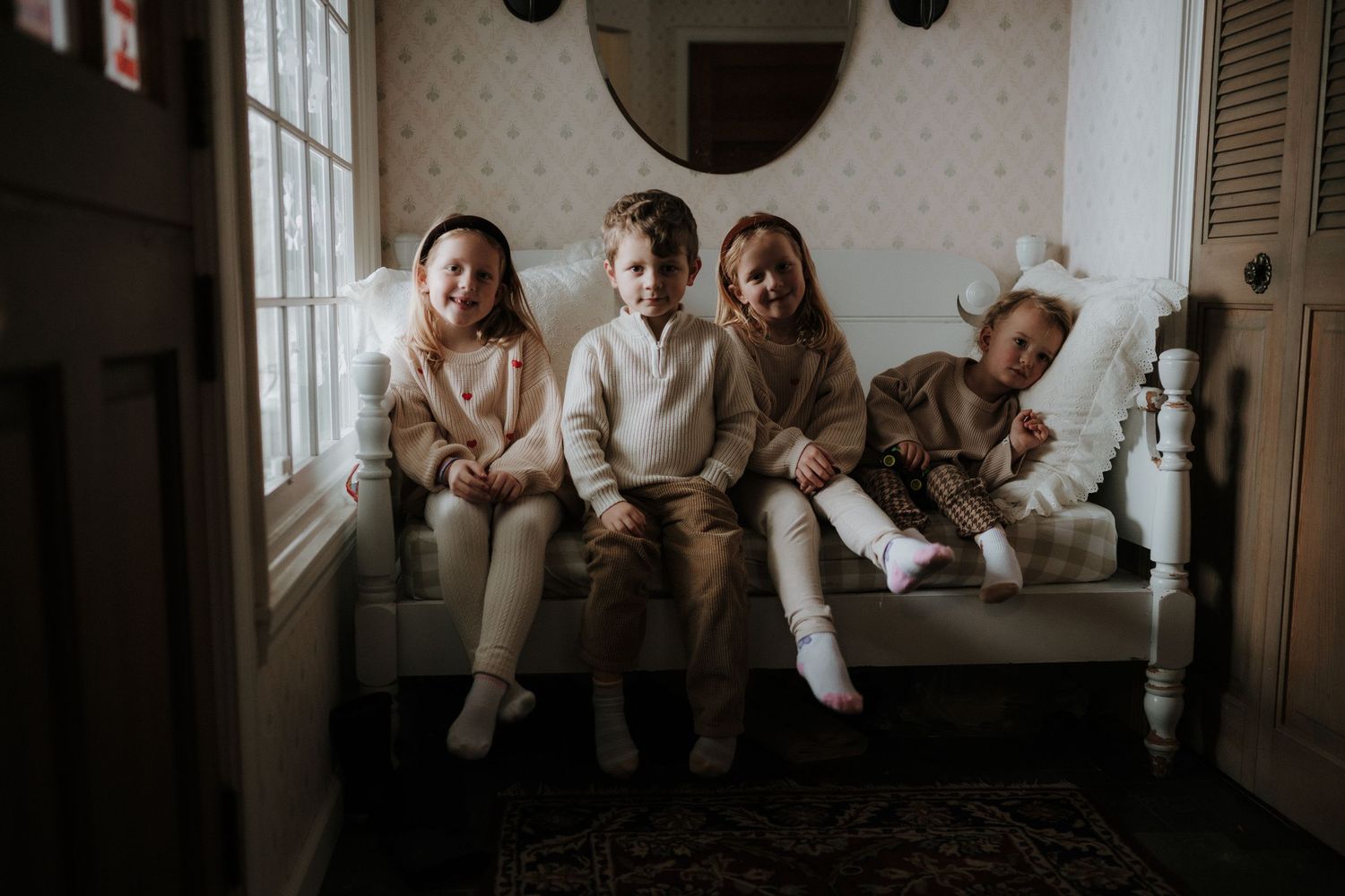 Children sit together on a window bench in coordinated neutral-colored outfits.