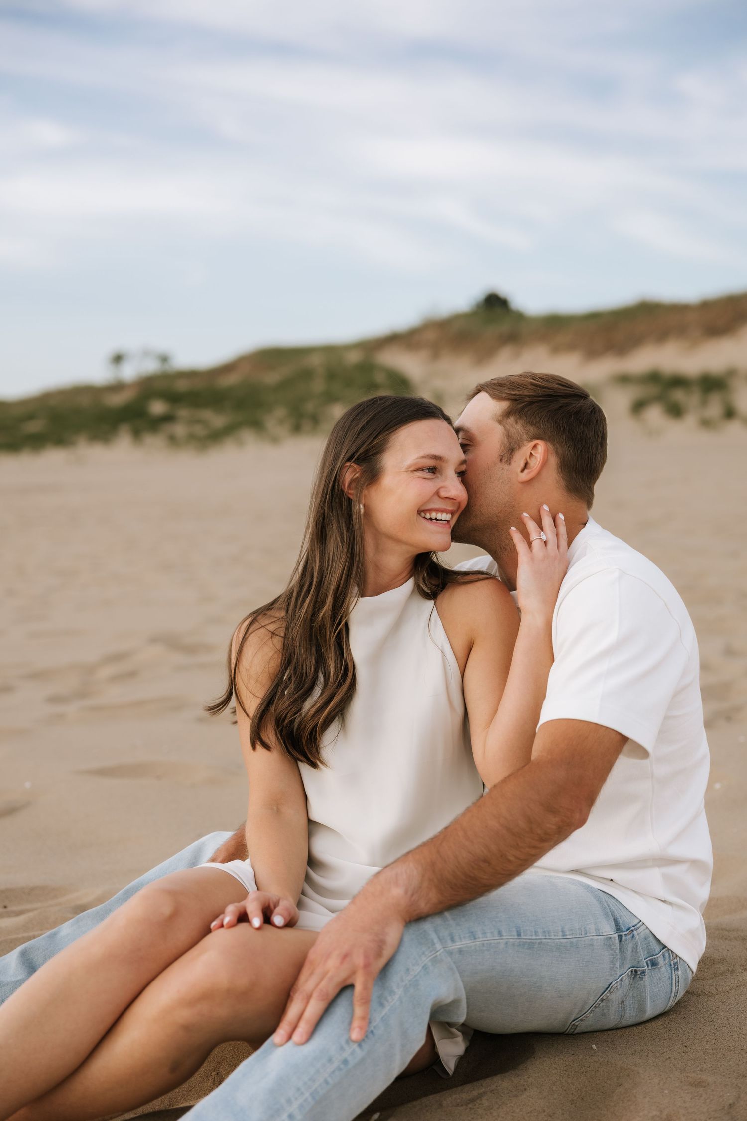 Romantic couple sitting on sandy beach, smiling and sharing an intimate moment together.