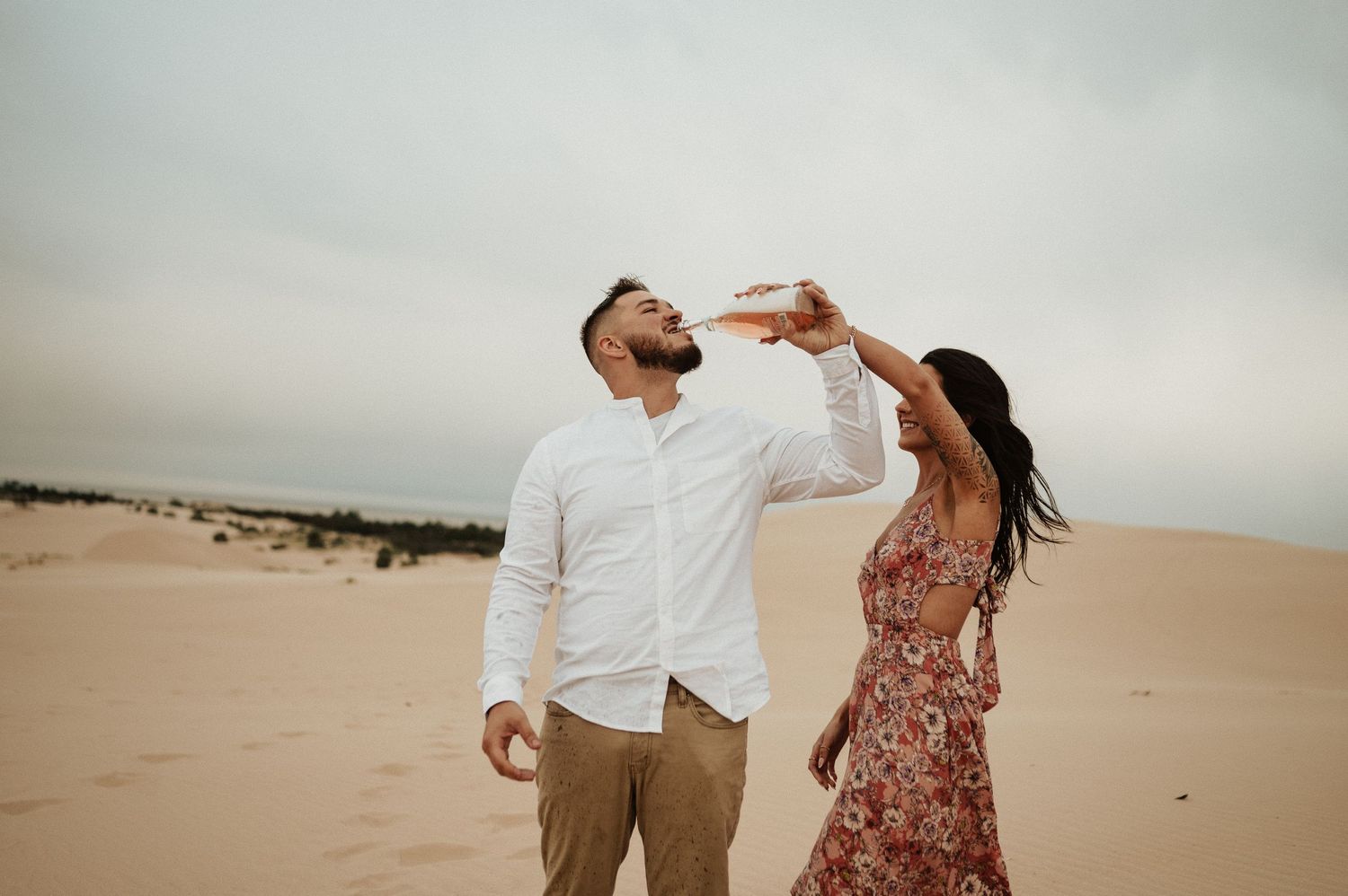 A playful couple poses together on sand dunes during a desert photoshoot.
