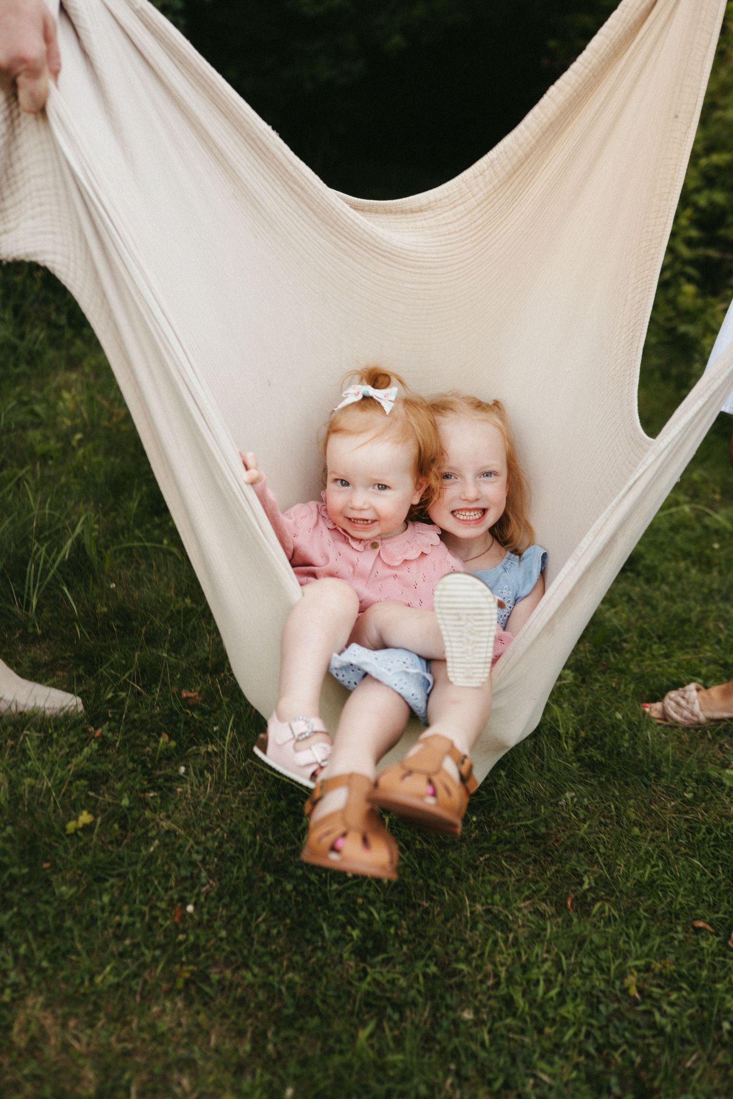 Two children sharing joyful laughter while relaxing together in a white hammock outdoors.