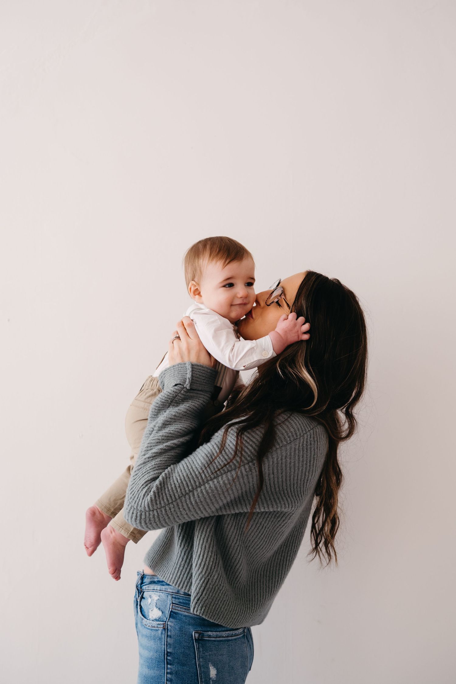 A tender moment between parent and child sharing cuddles in a gray sweater against white wall.