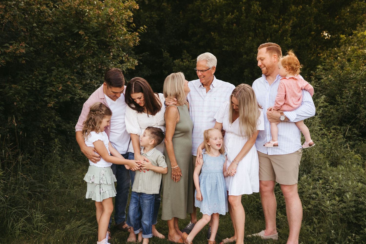 Extended family poses in coordinated pastel outfits during golden hour outdoor photography session.