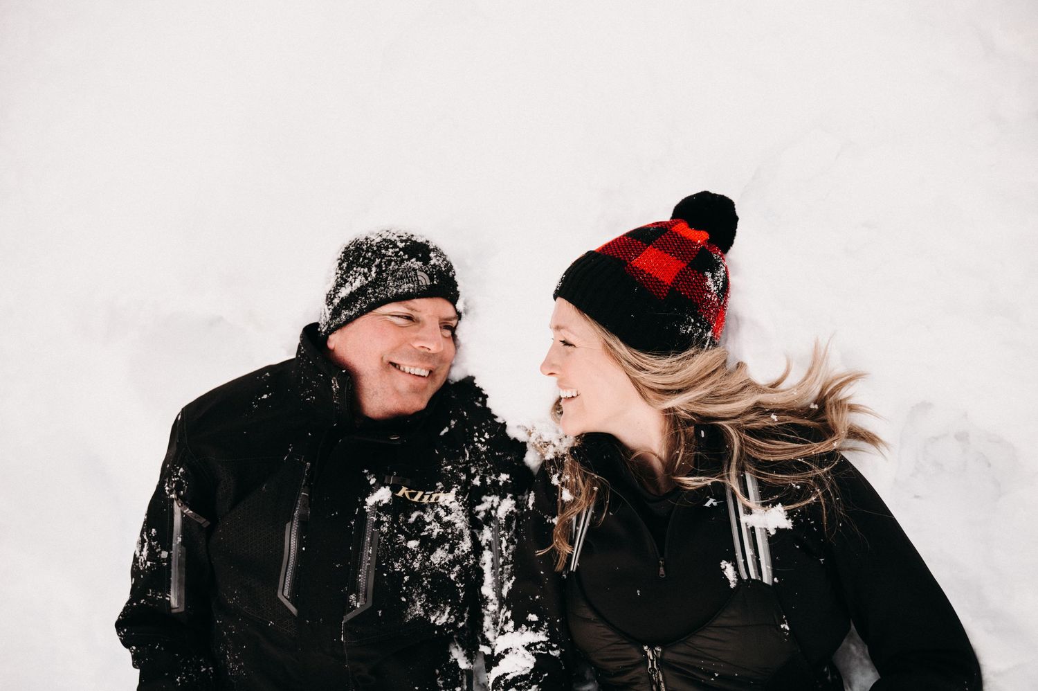 A couple in winter clothing sharing laughter in the snow.