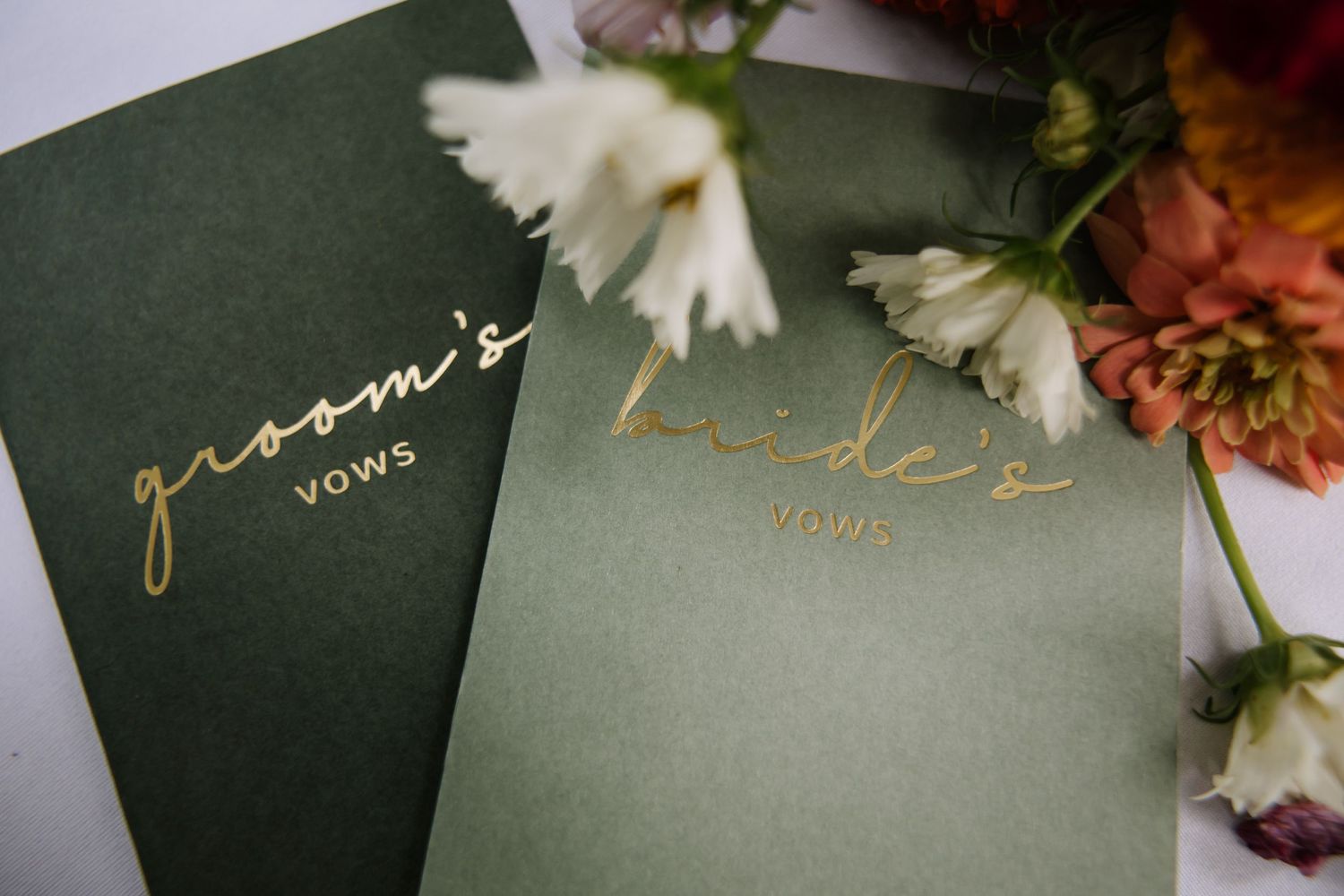 Wedding invitation suite featuring elegant gold calligraphy on dark green paper with floral accents.