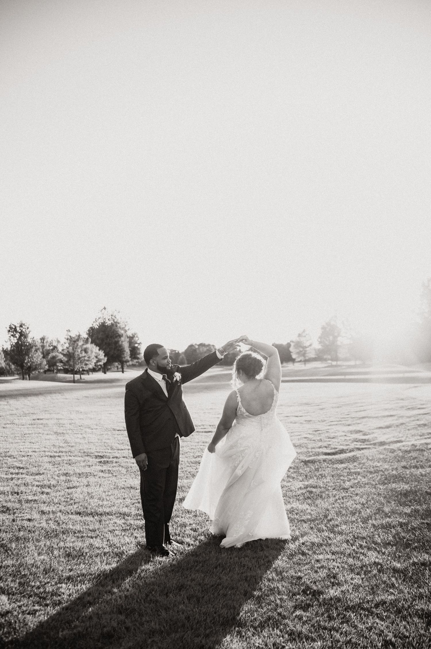 Black and white silhouette of couple dancing in an open field during golden hour.