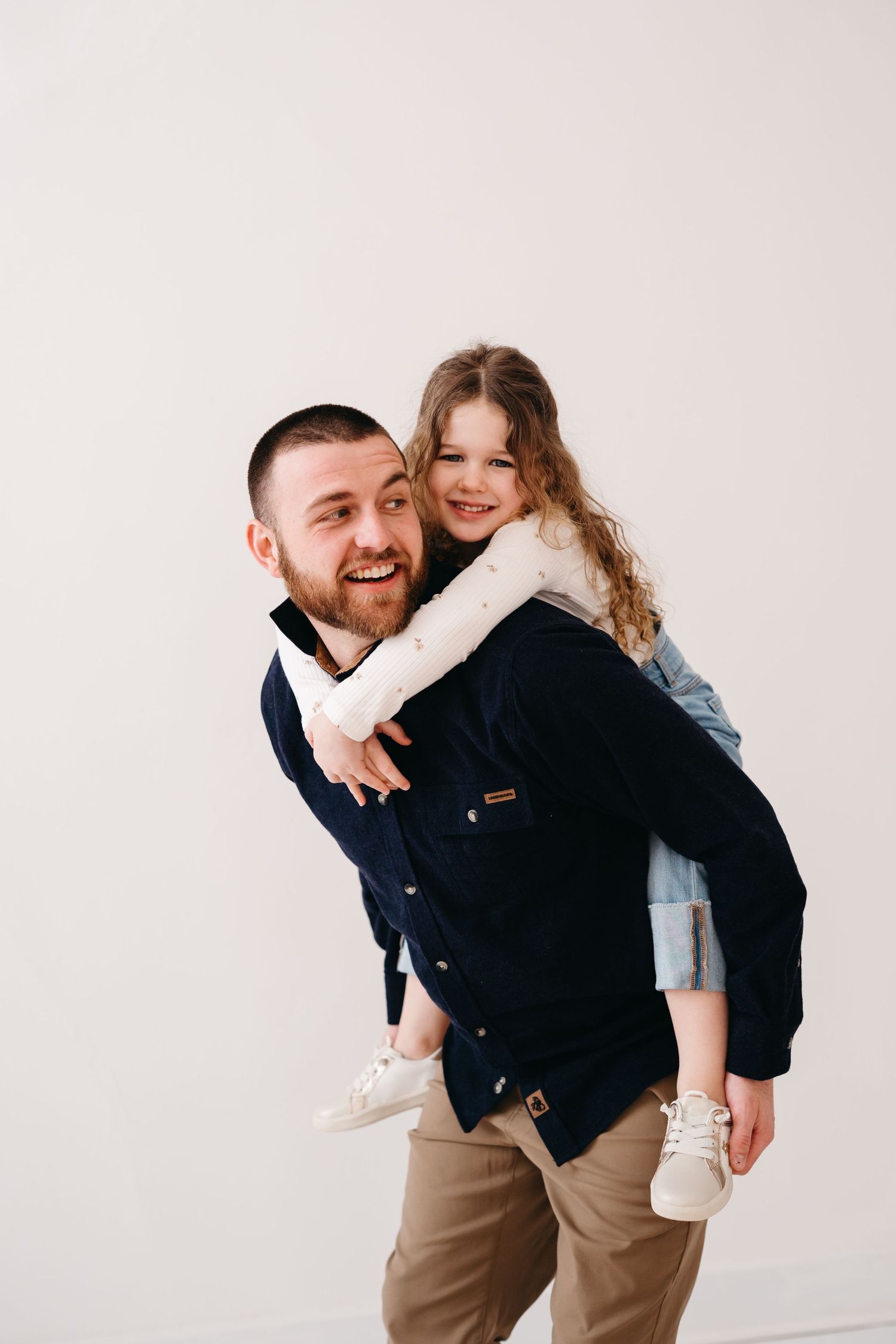 Playful indoor portrait with piggyback ride against white background.