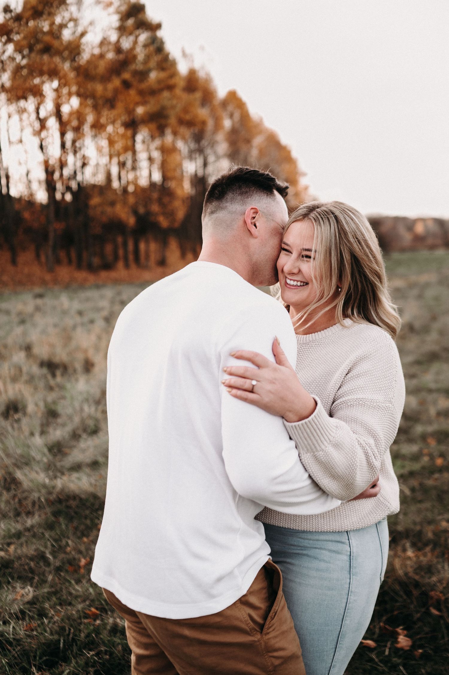 Joyful couple embracing and laughing in autumn field setting.