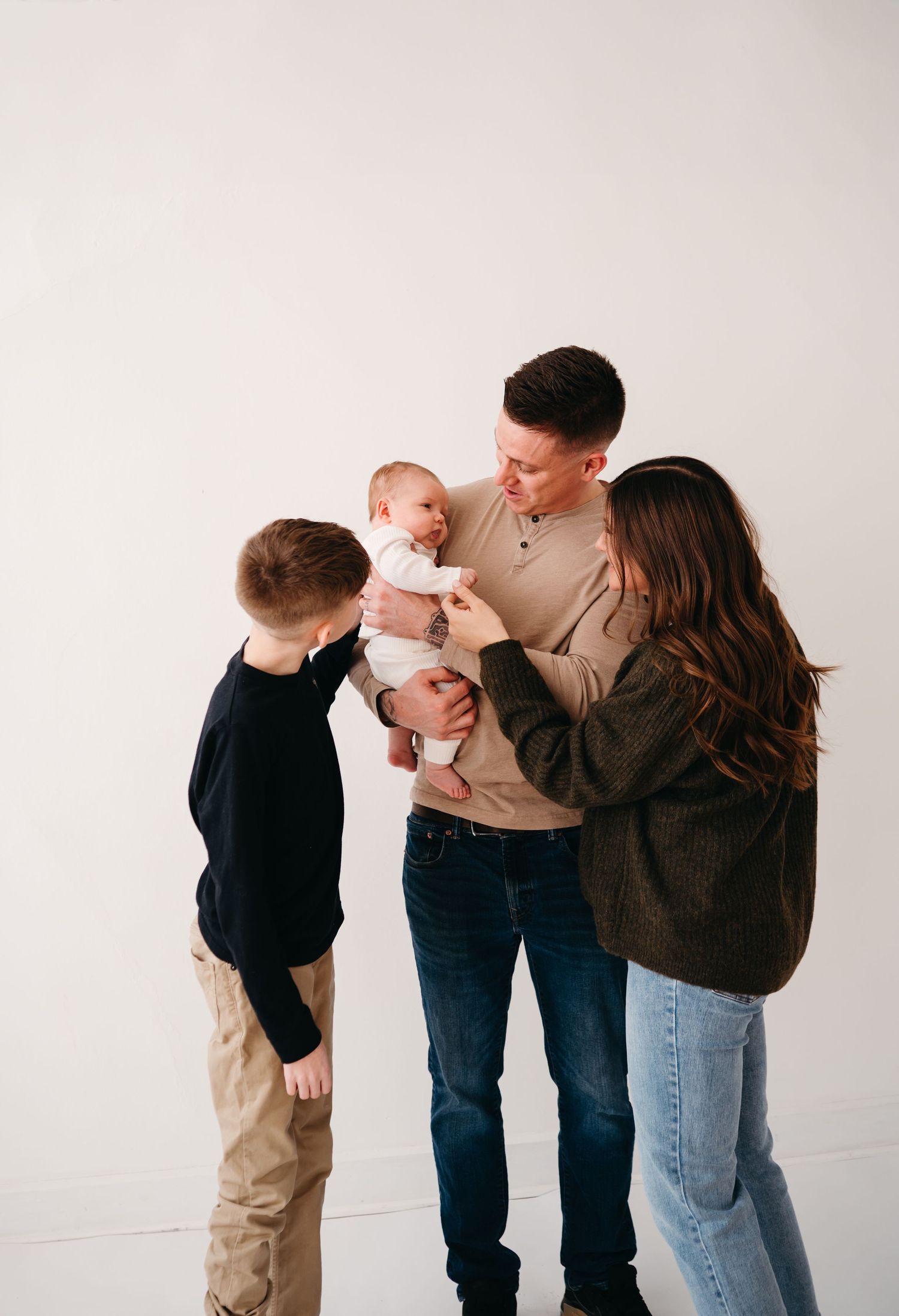 A family of four shares a tender moment together against a white backdrop.