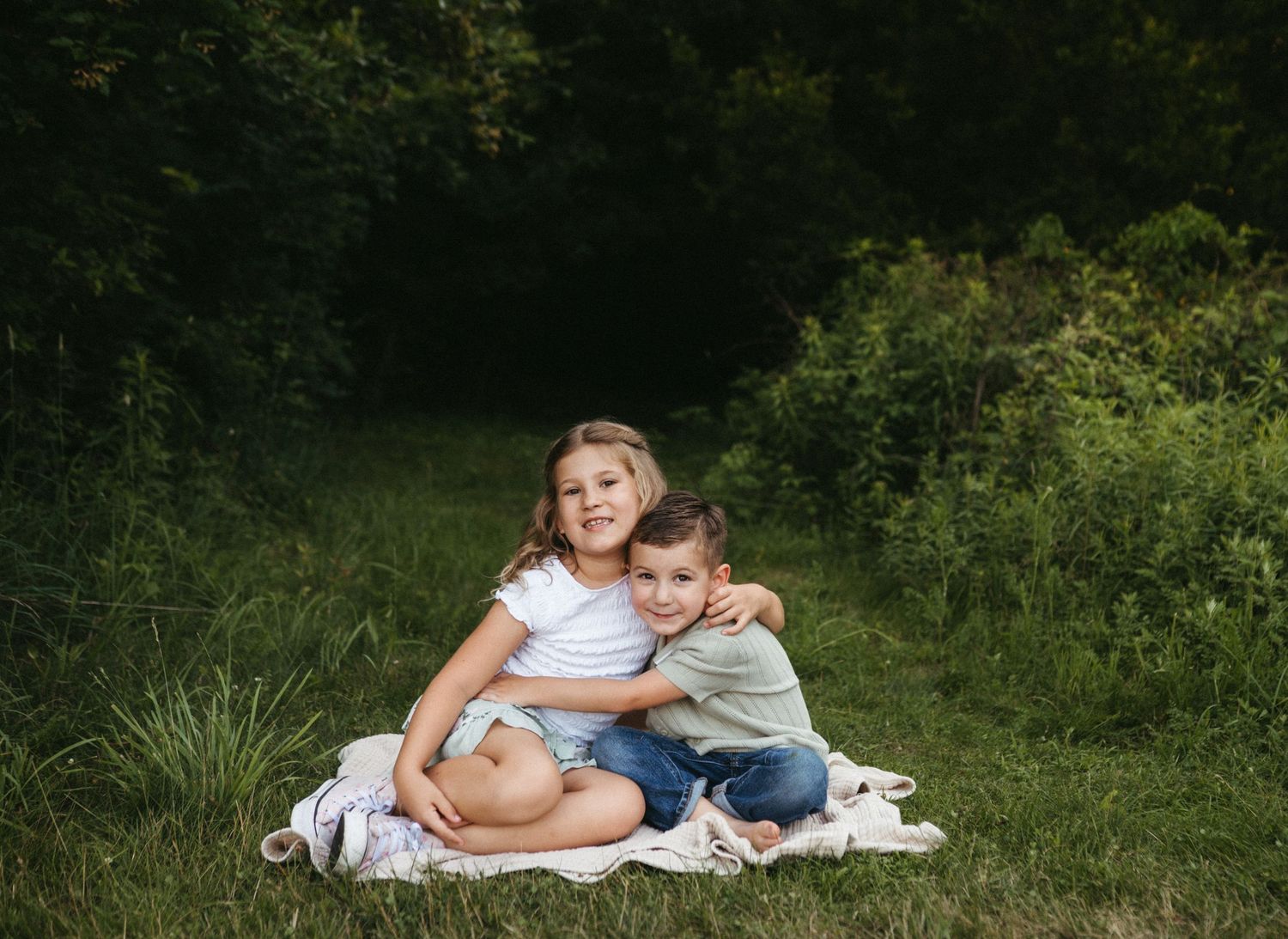 Candid lifestyle portrait of people relaxing on a blanket in a grassy outdoor setting.
