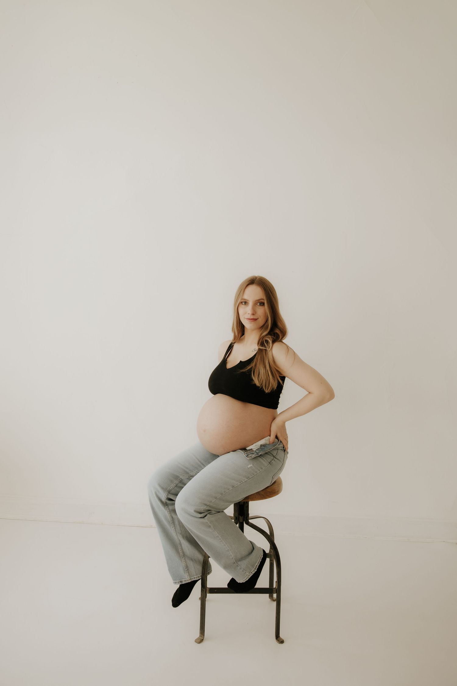 Artistic maternity portraits on a white backdrop featuring poses on a black chair.