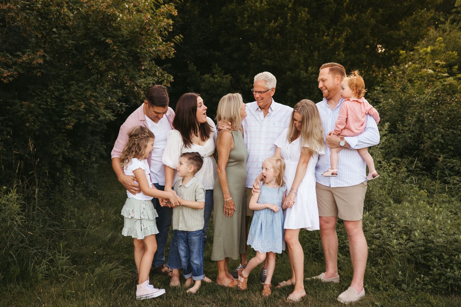 A family group in casual summer clothing gathered outdoors against a natural wooded backdrop.