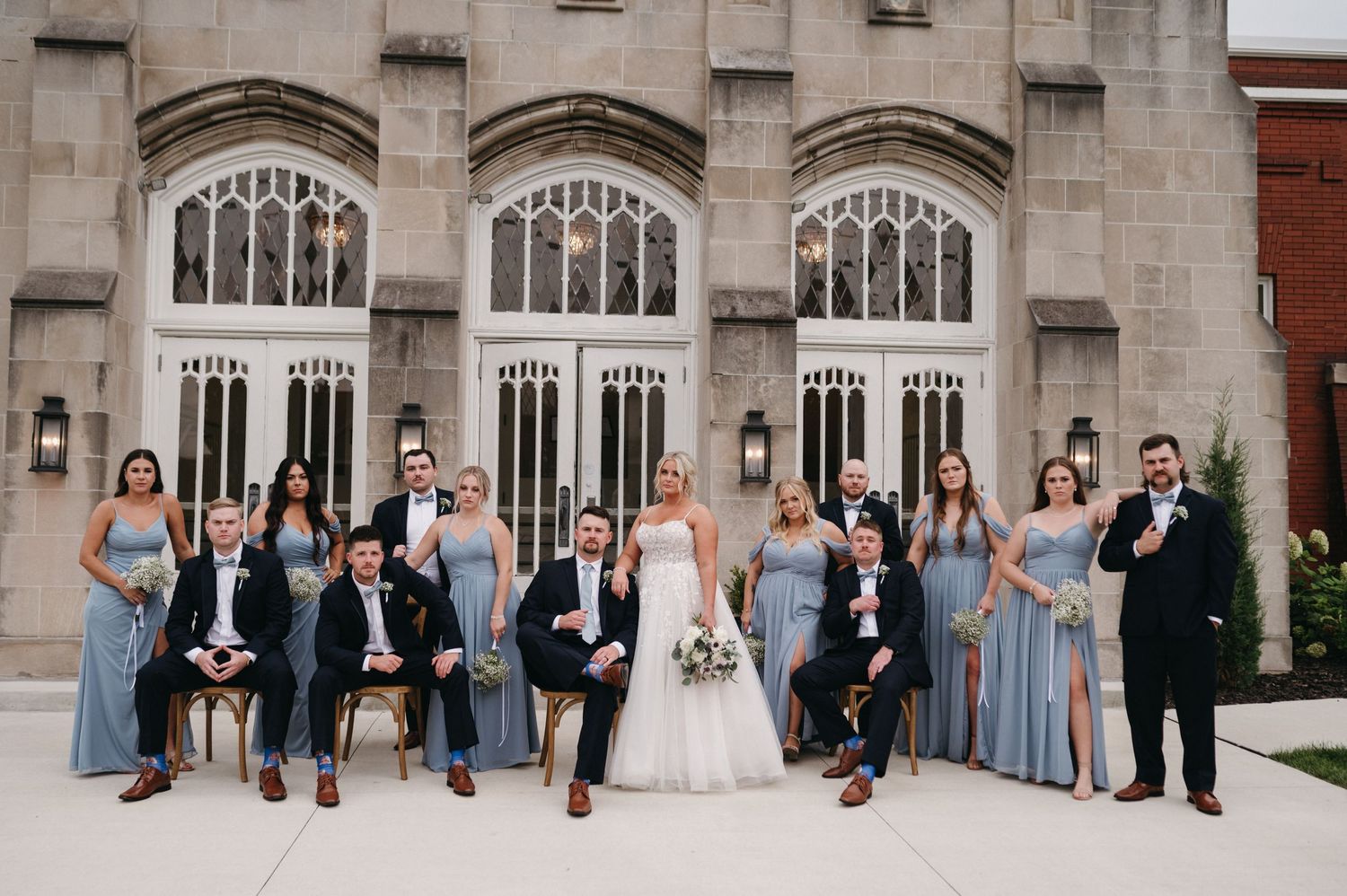 Full wedding party portrait with bridesmaids in blue dresses against Gothic church architecture.