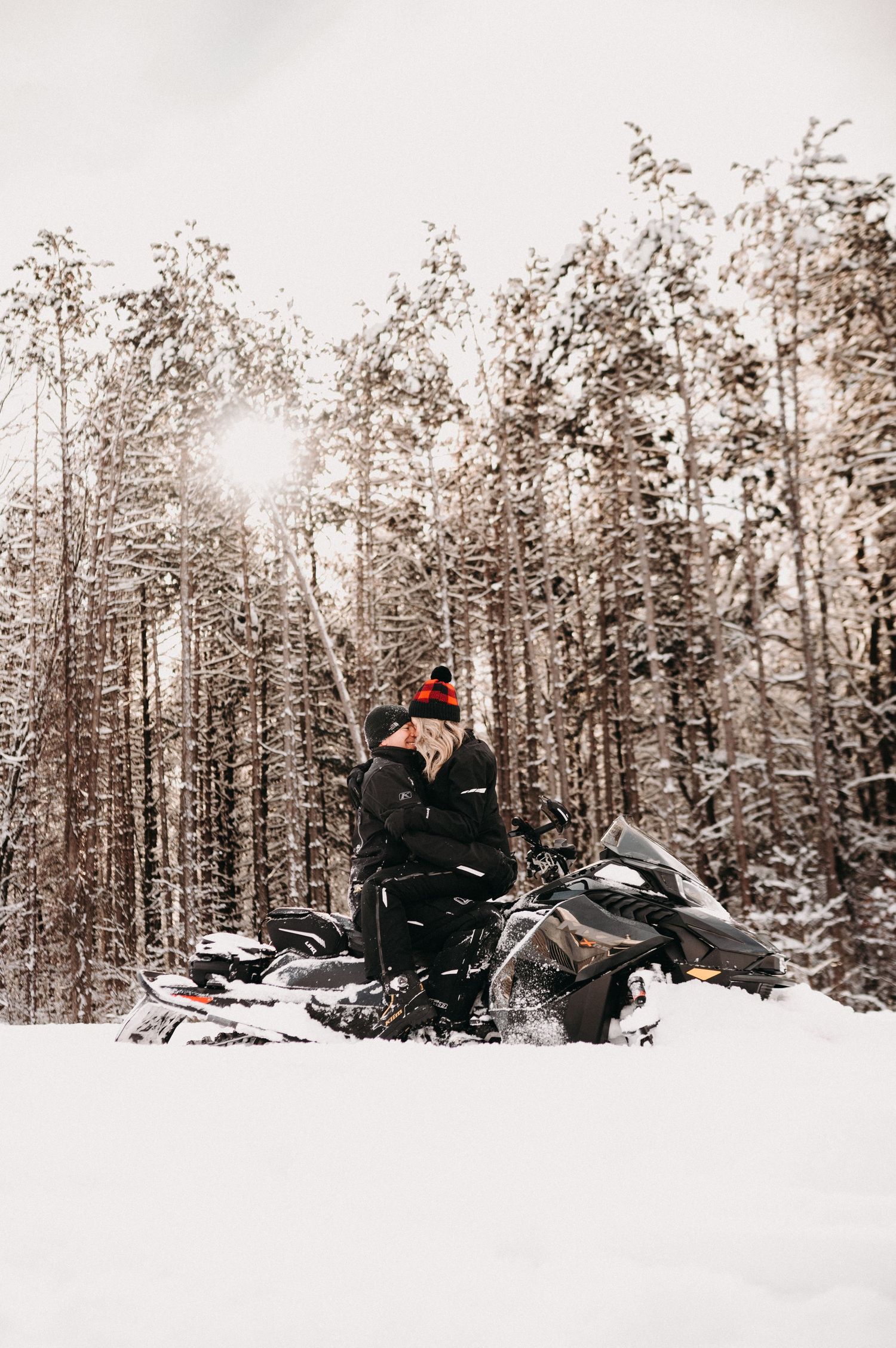 A person in winter gear sitting on a snowmobile in a snowy forest.