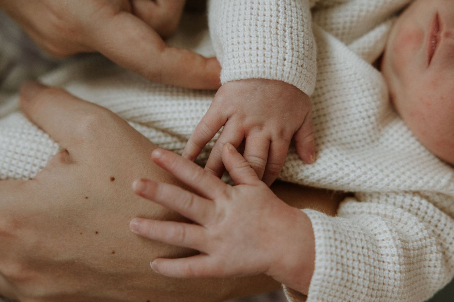 Close-up of small and large hands touching on white knit fabric.