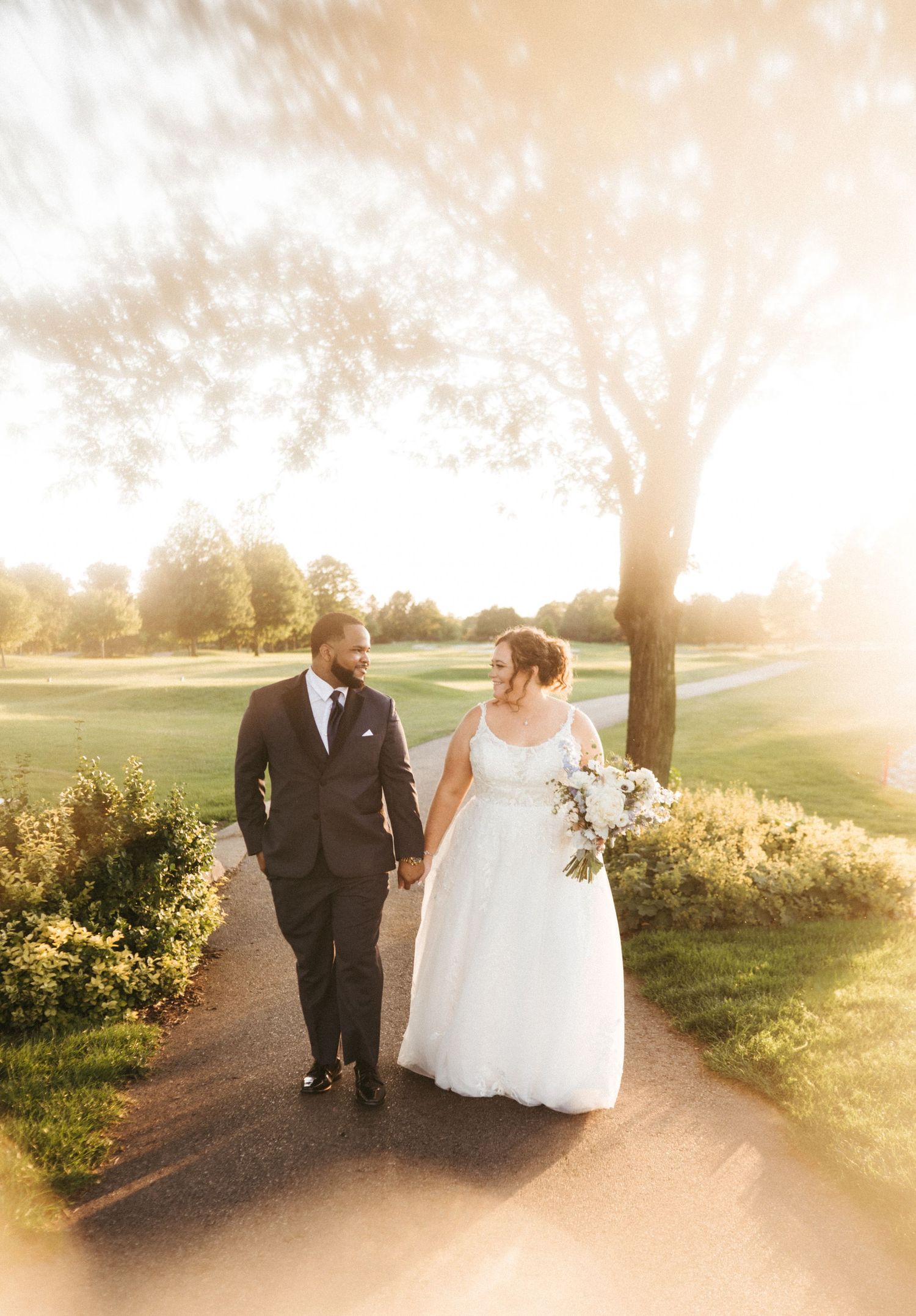 Wedding couple walking along tree-lined path during golden sunset.
