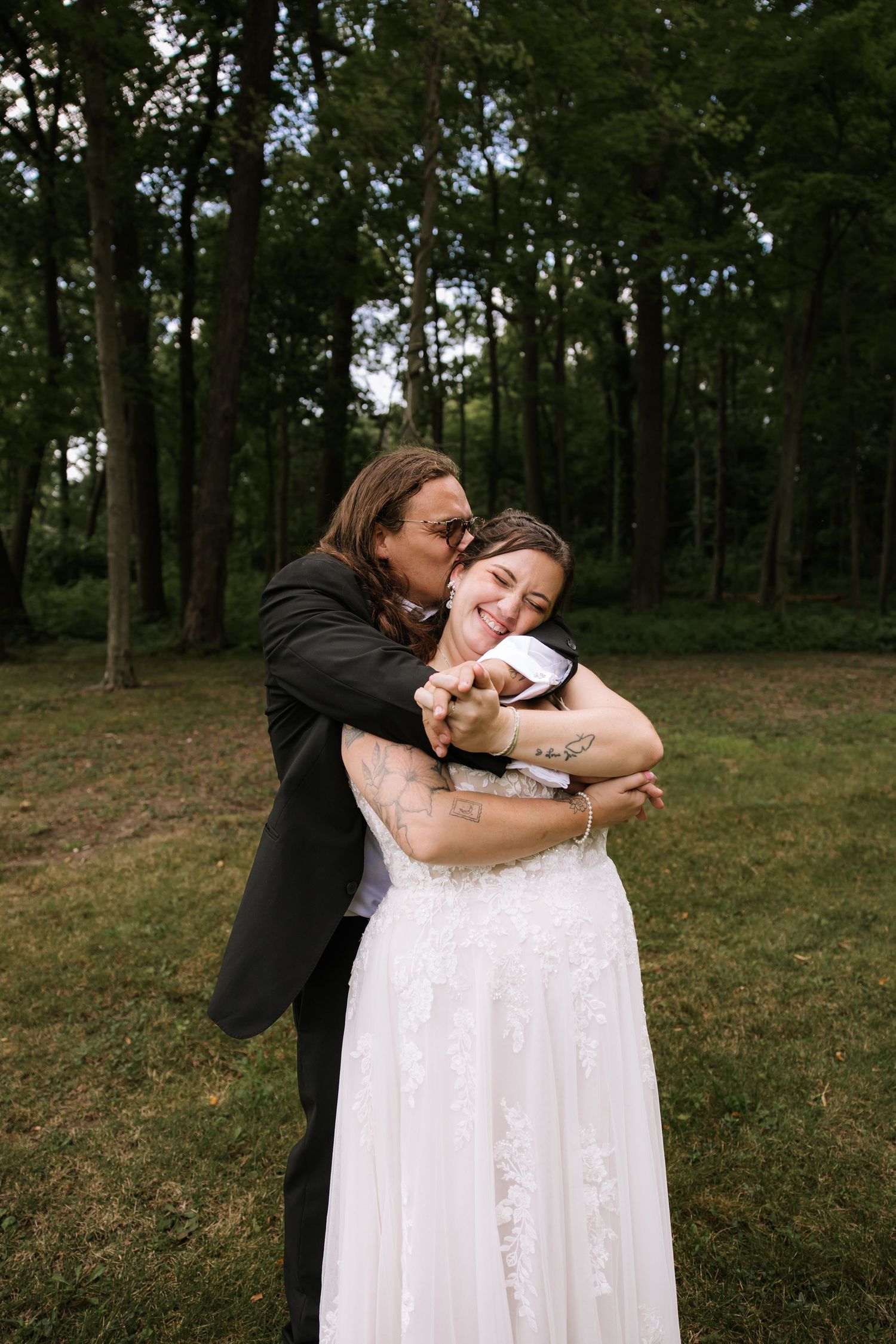 A couple shares a tender moment during their wedding photoshoot in a forest setting.
