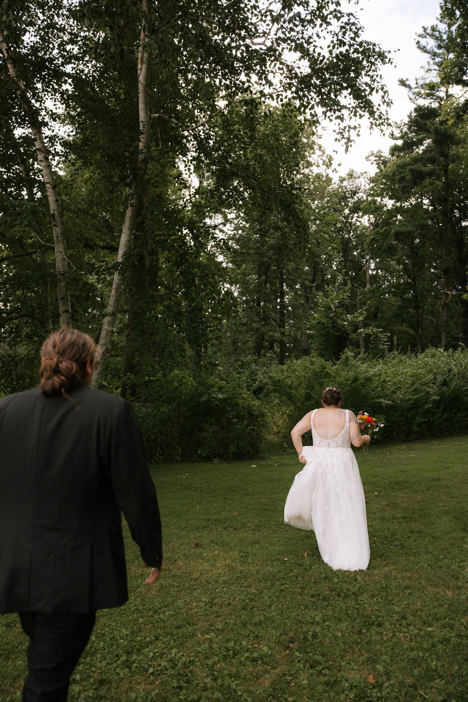 A couple walks hand in hand across a grassy lawn surrounded by trees during an outdoor event.