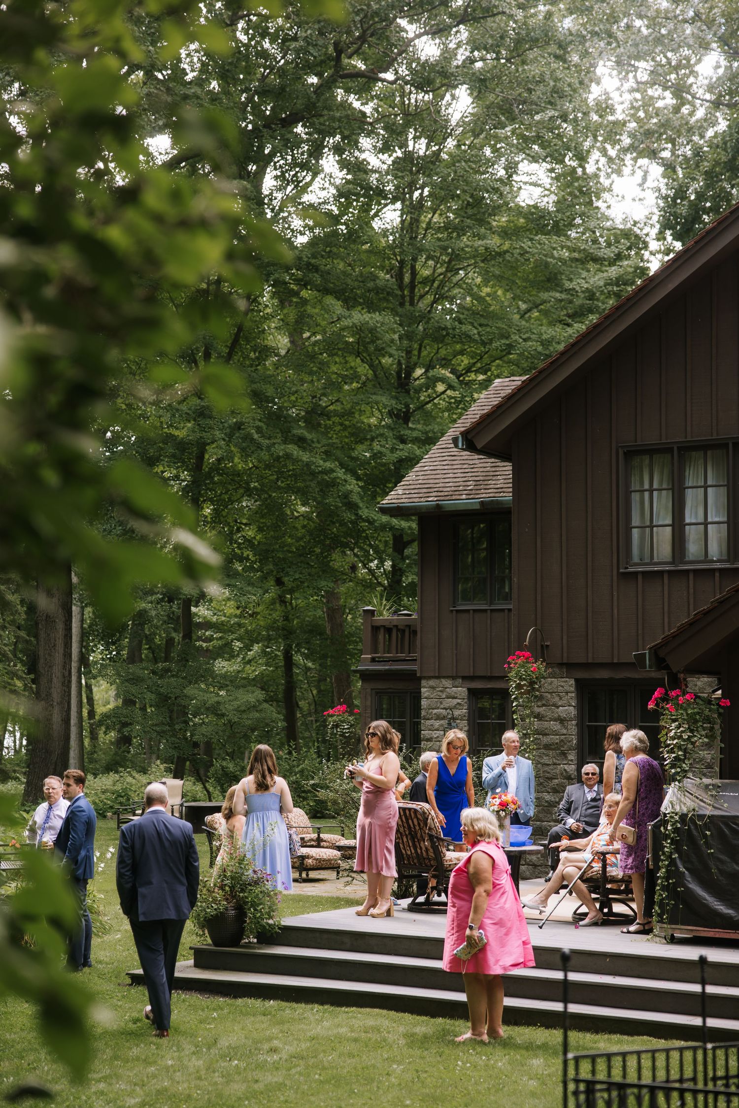 Wedding guests gather outside rustic brown cabins decorated with hanging flower baskets.