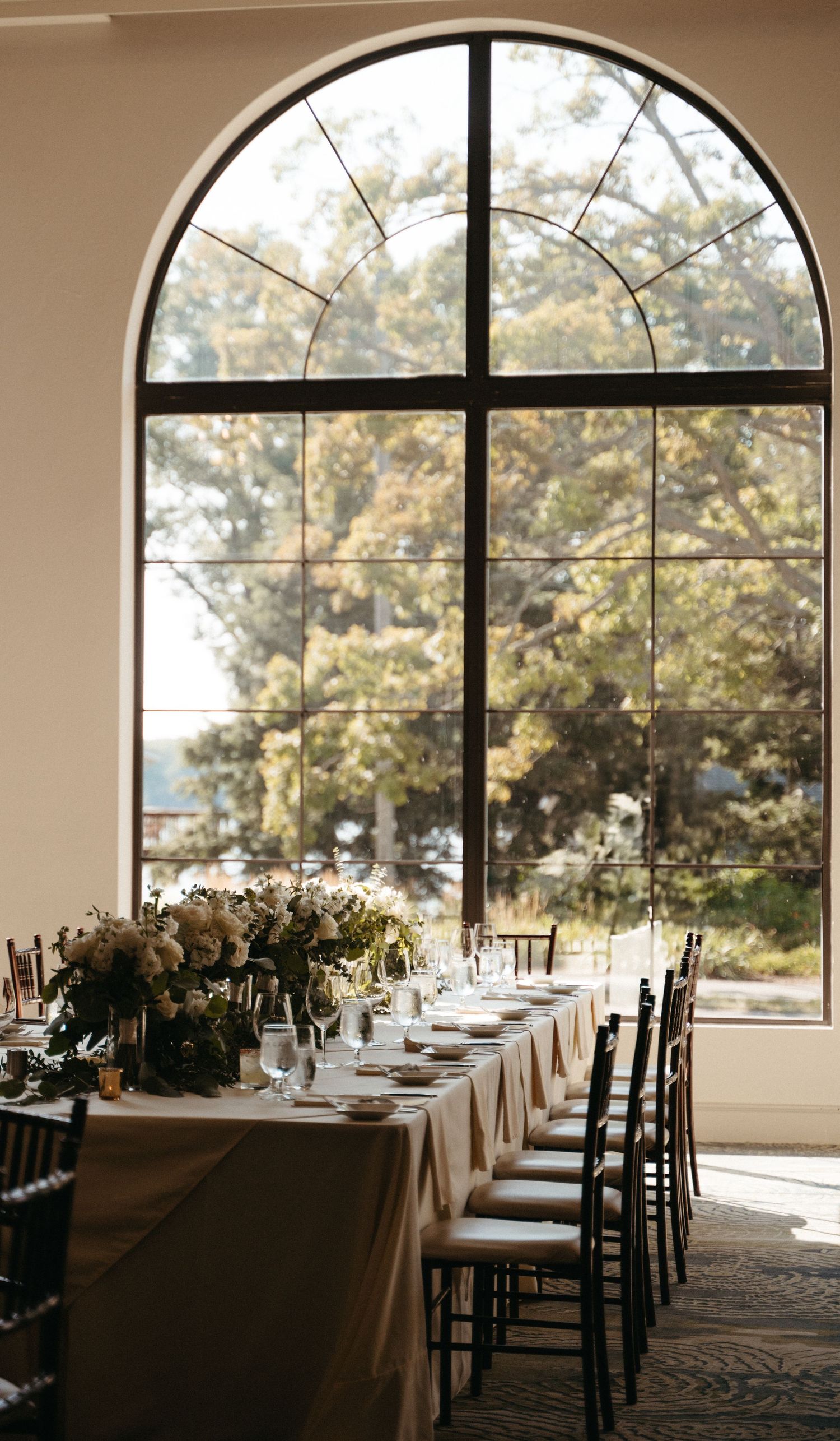 Elegant wedding reception table set beneath a grand arched window with natural light streaming in.