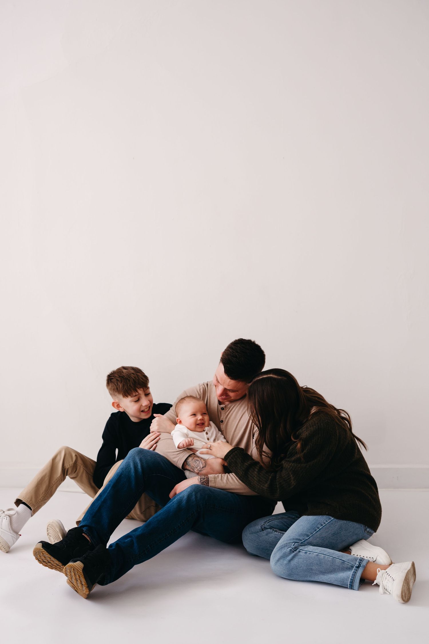 A family sits close together on a white floor wearing casual clothing in jeans and sweaters.