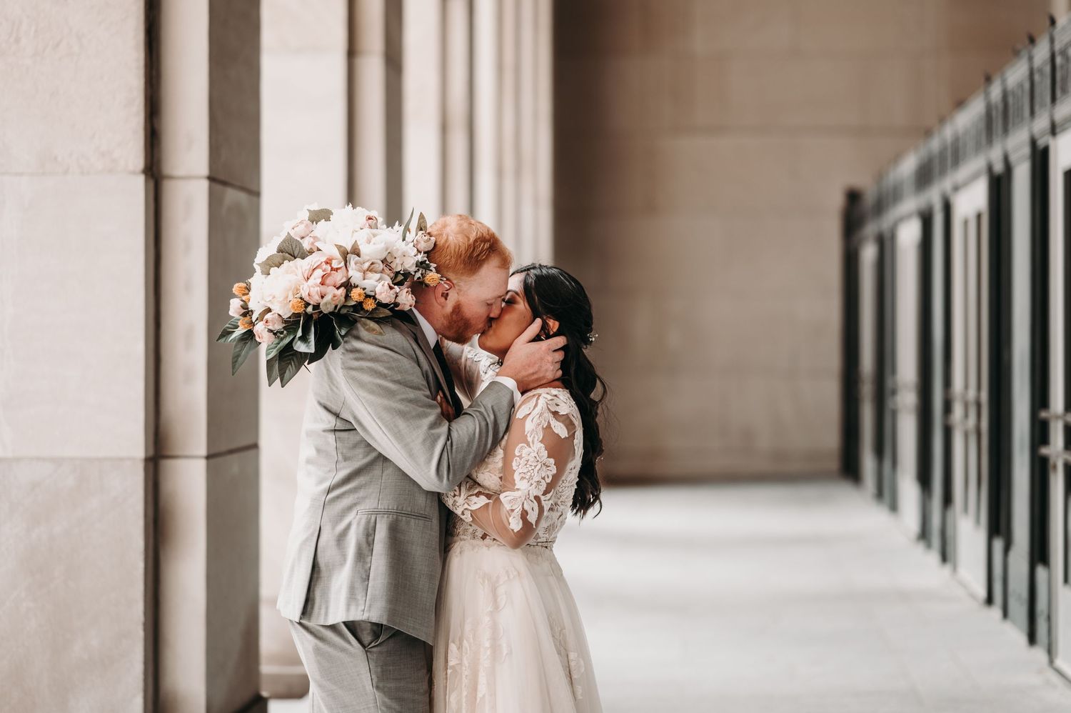 Wedding couple sharing intimate moment under stone archway with floral bouquet.