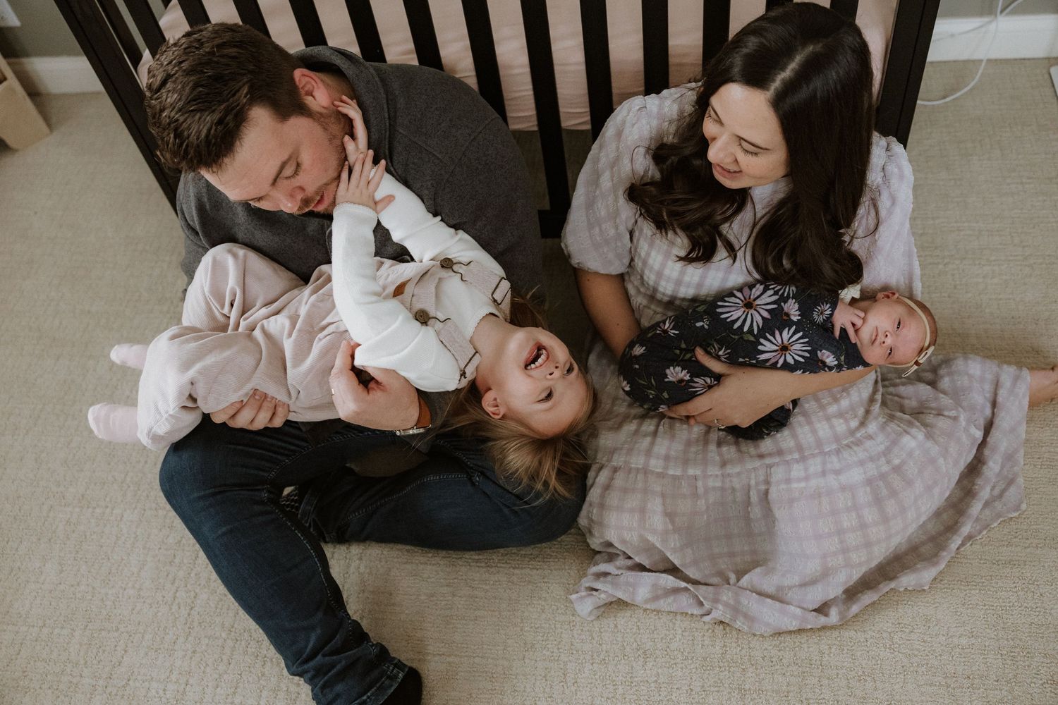 A family relaxes together on a carpeted floor, laughing and playing with their pets in a joyful candid moment.
