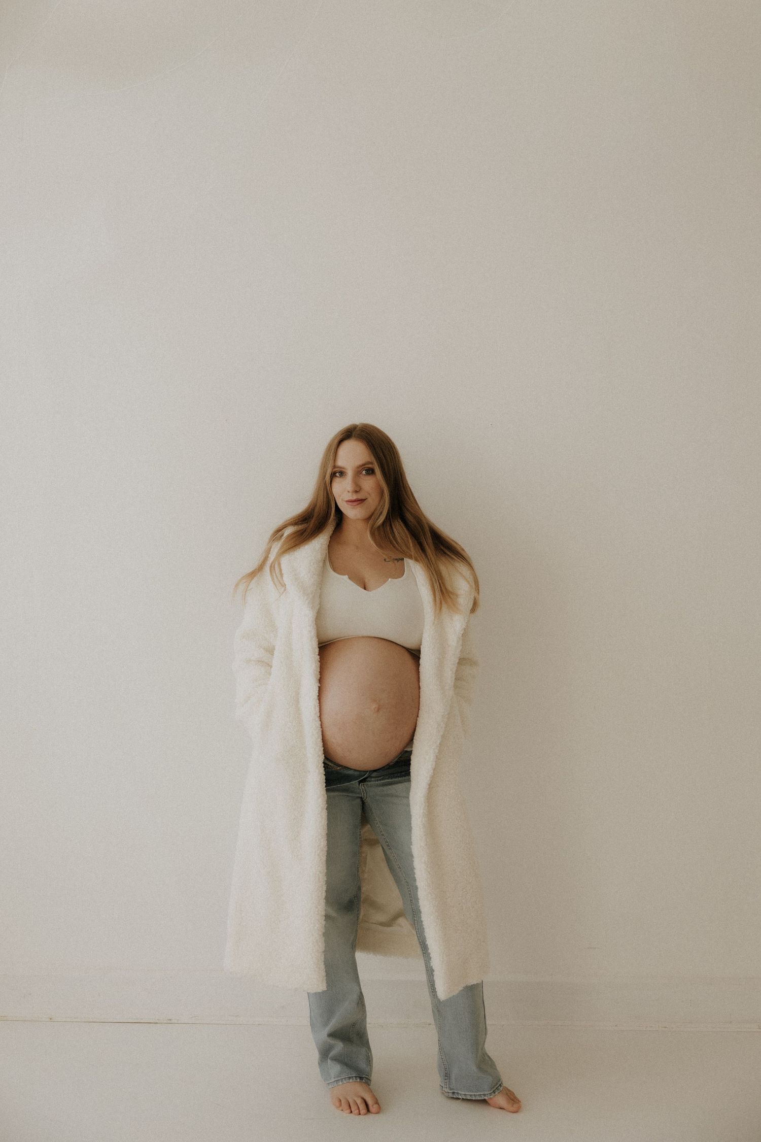 Modern maternity photography with woman in casual denim and white coat.