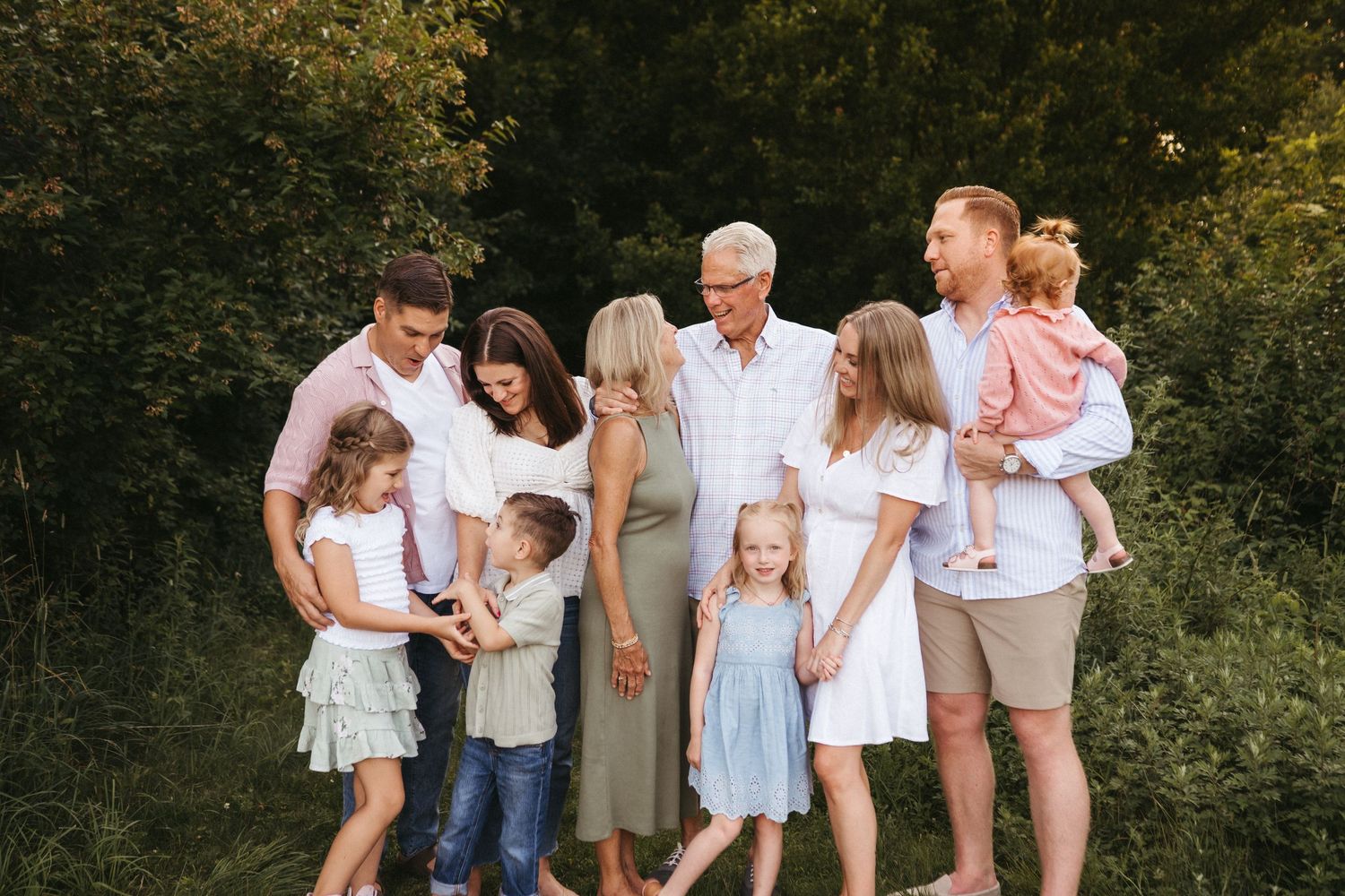 A multi-generational group poses together outdoors wearing coordinated casual outfits in neutral tones.