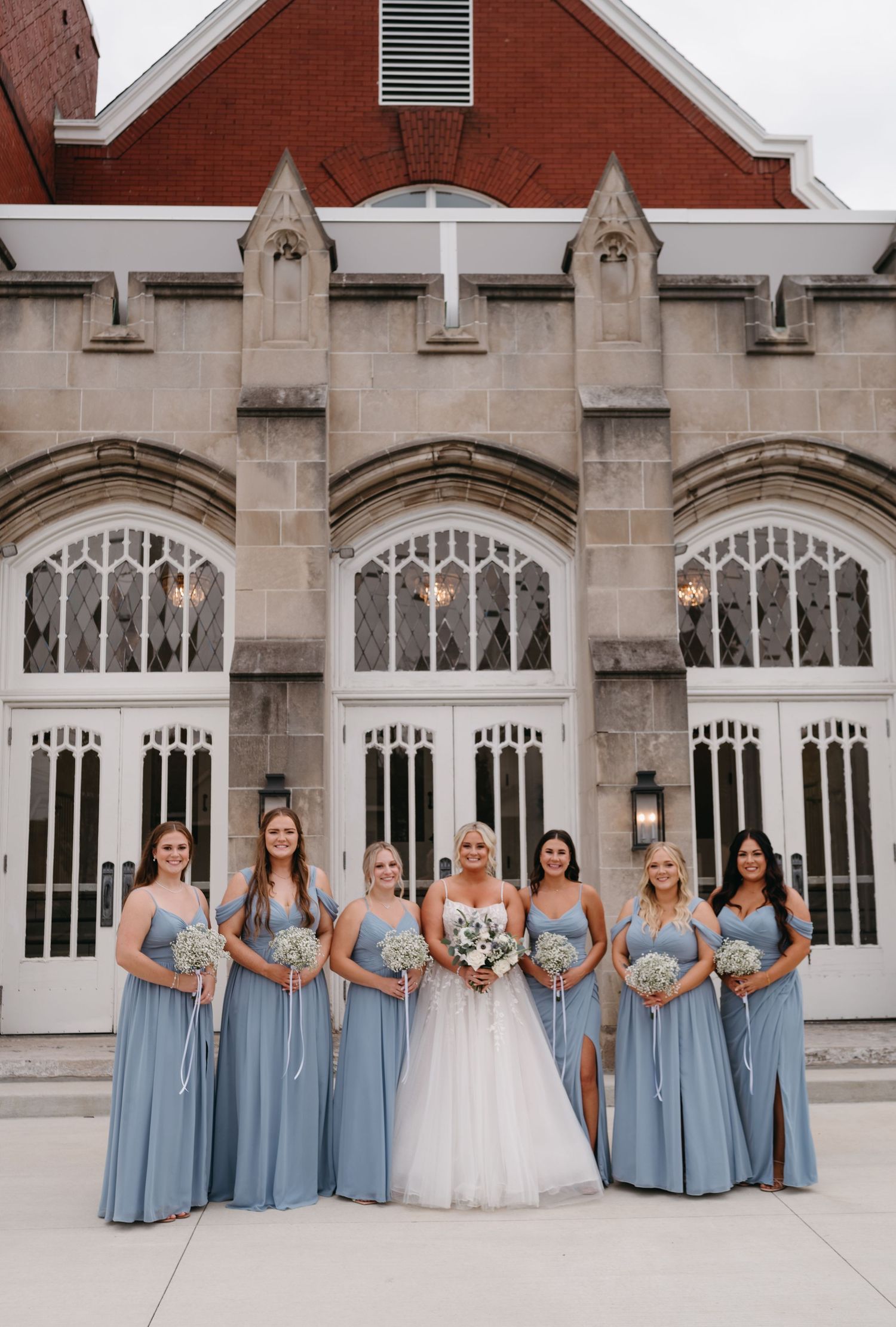Wedding party in powder blue dresses poses in front of Gothic church architecture.