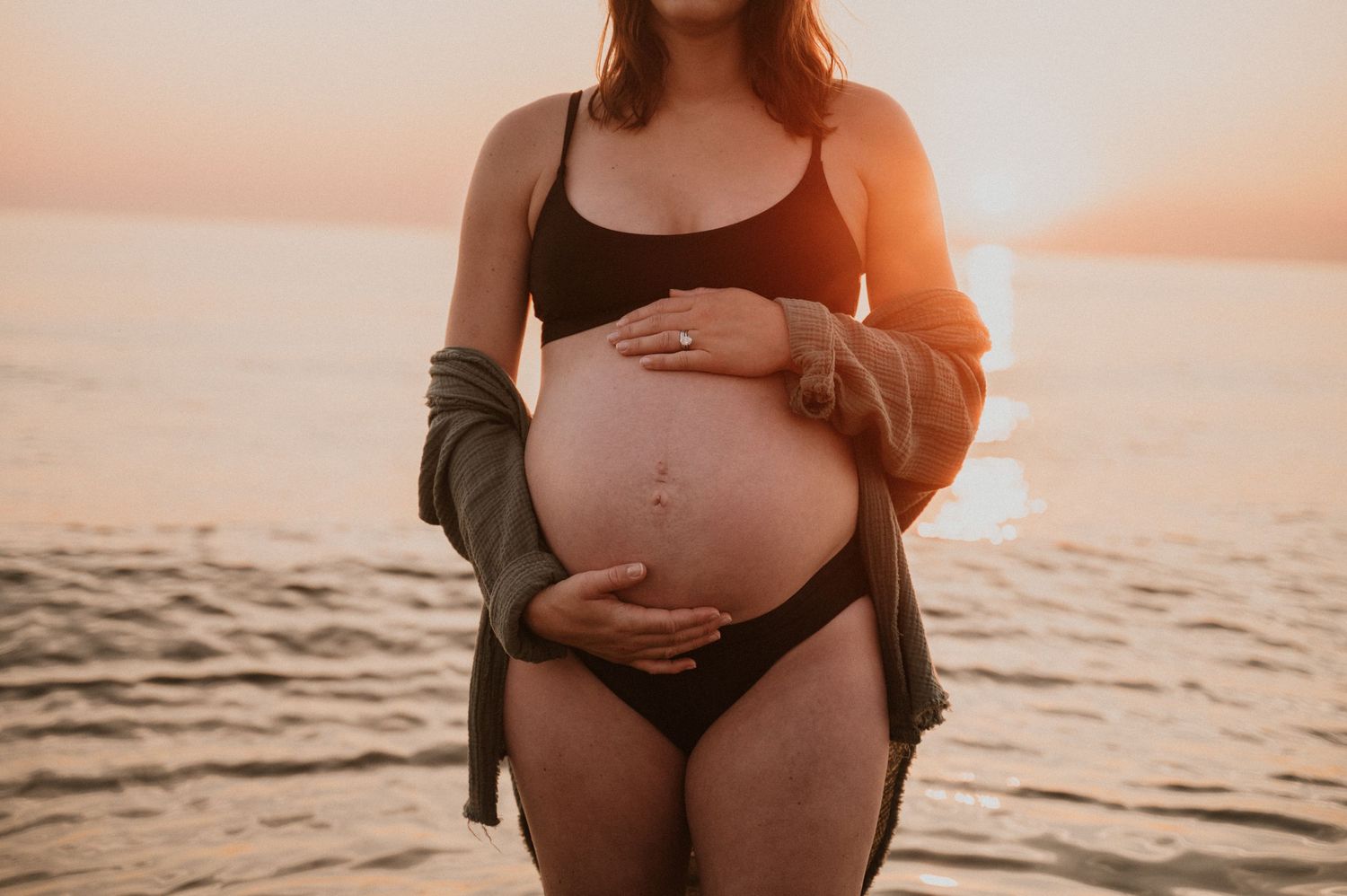 Maternity photo capturing tender moment at sunset with ocean backdrop.