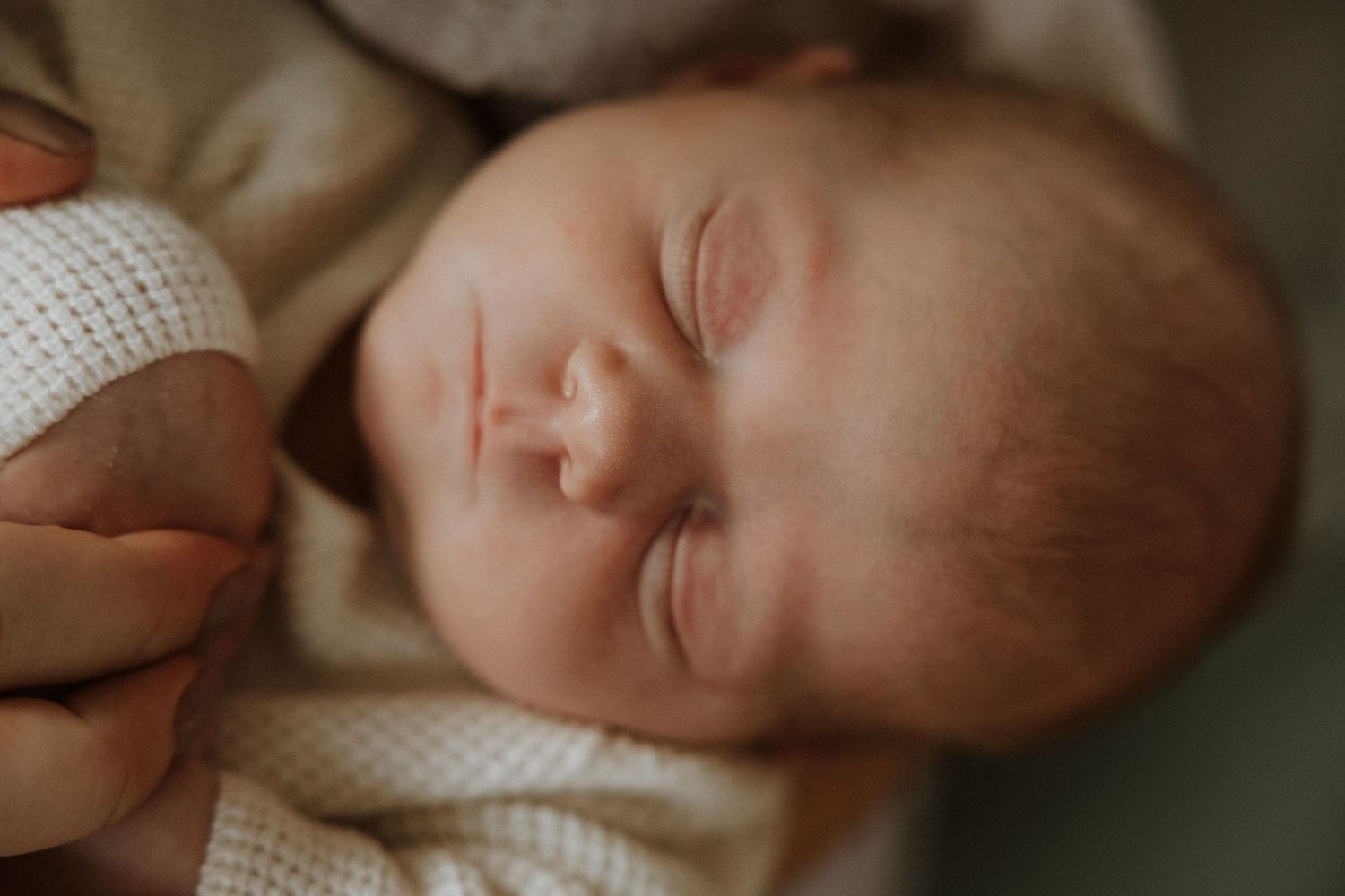 Peaceful sleeping newborn baby wrapped in white knit blanket.