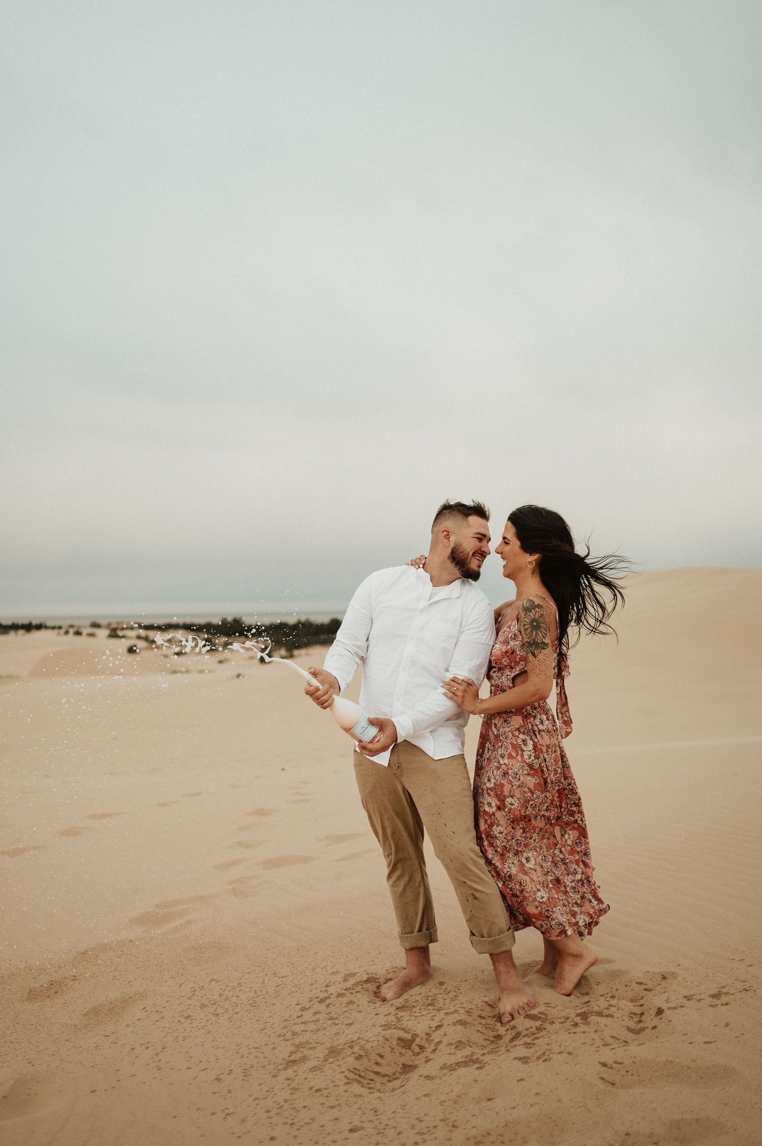 A couple embraces while walking together on desert sand dunes under cloudy skies.