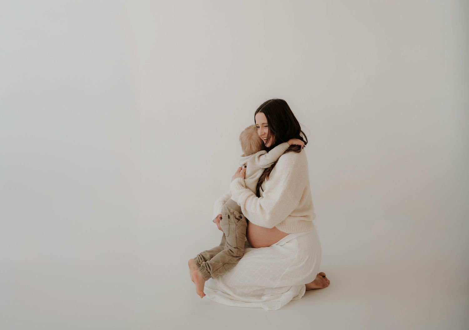 A figure in white clothing holds a small child against a minimalist background.