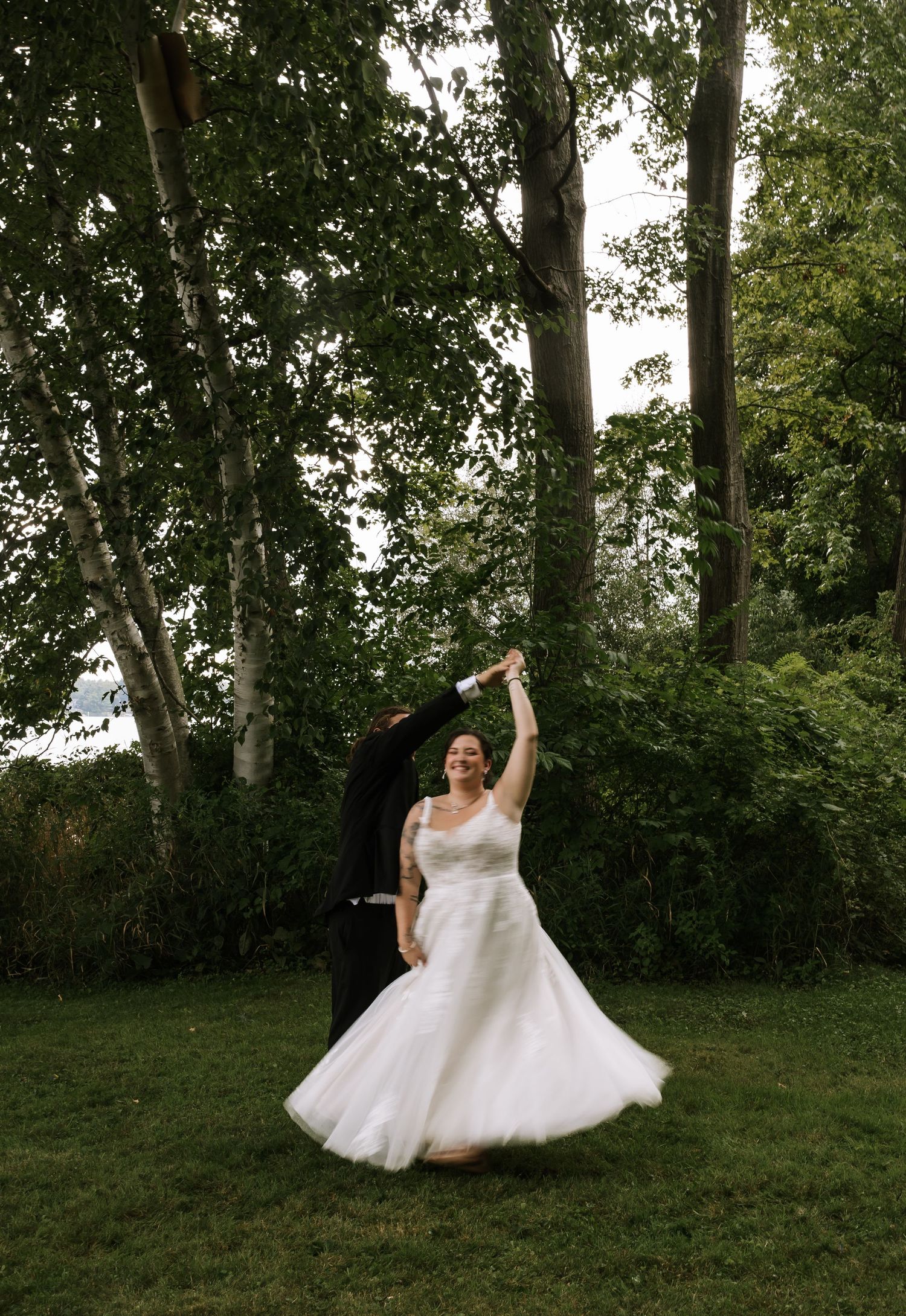 A bride twirls in her flowing white dress during an outdoor photo session among trees.