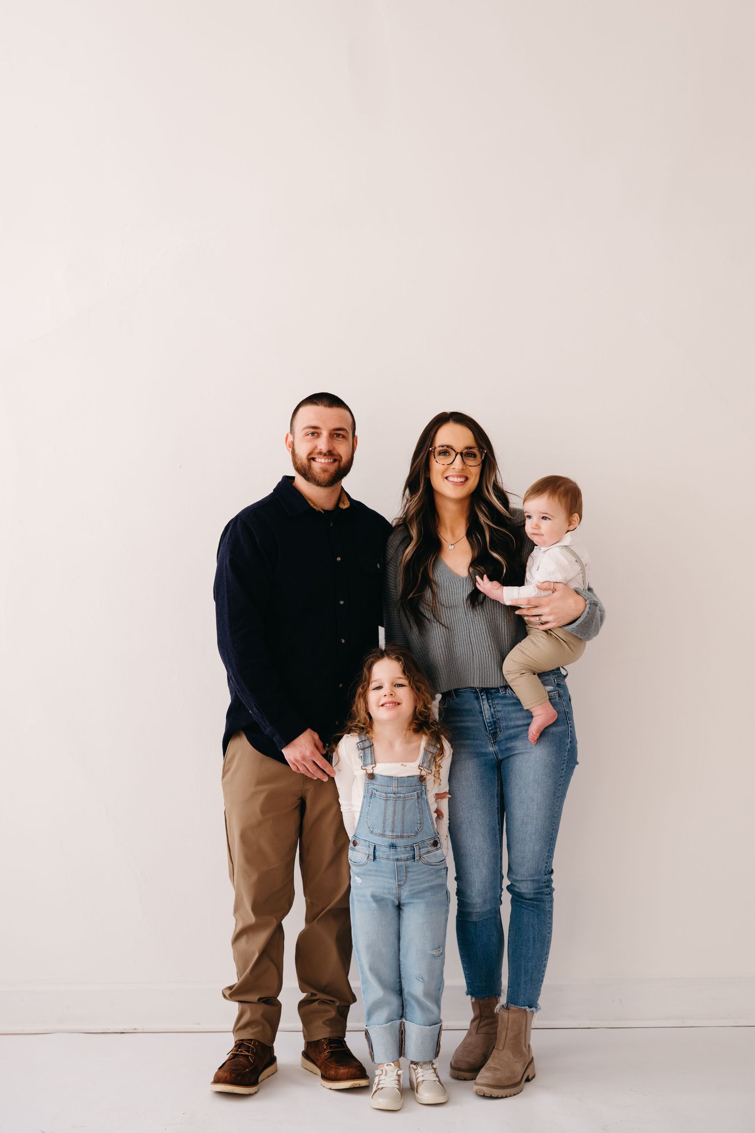 A family of four stands close together posing for a portrait against a white wall background.