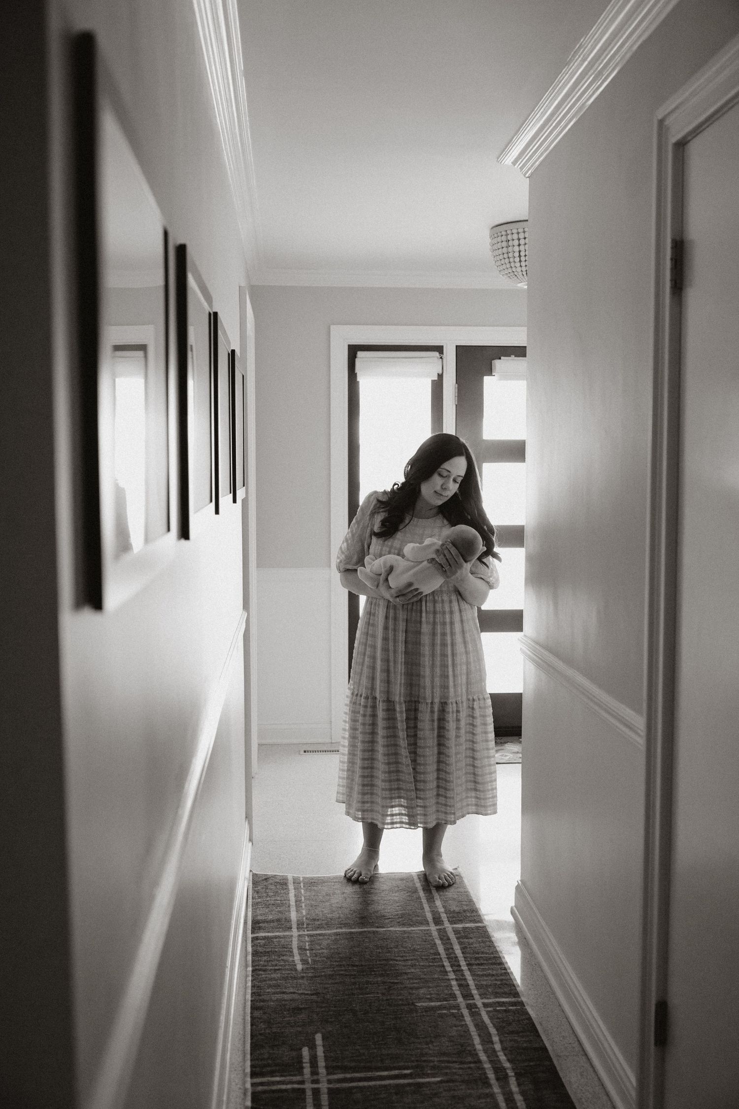 A tender moment captured in black and white as a figure stands in a sunlit hallway.
