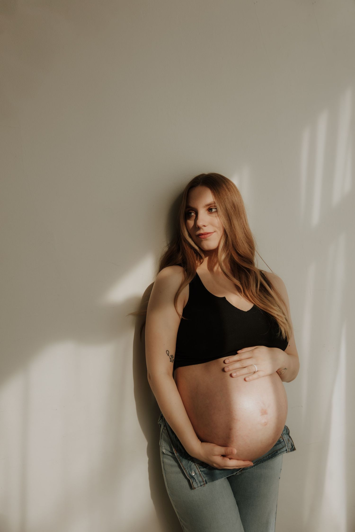 Minimalist maternity photography showcasing pregnant belly against light beige wall.