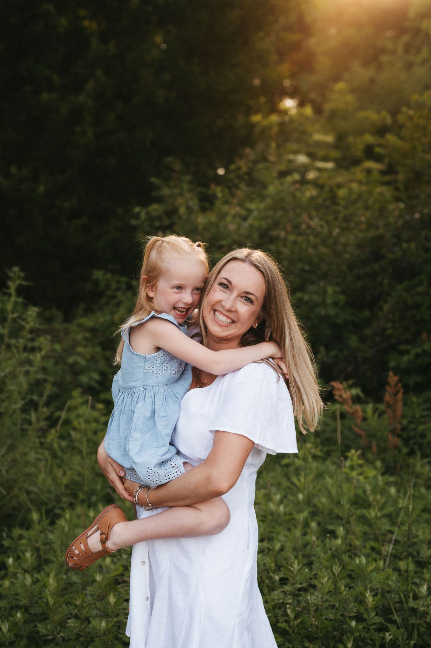 Tender moment between parent and child hugging outdoors in summer evening light.